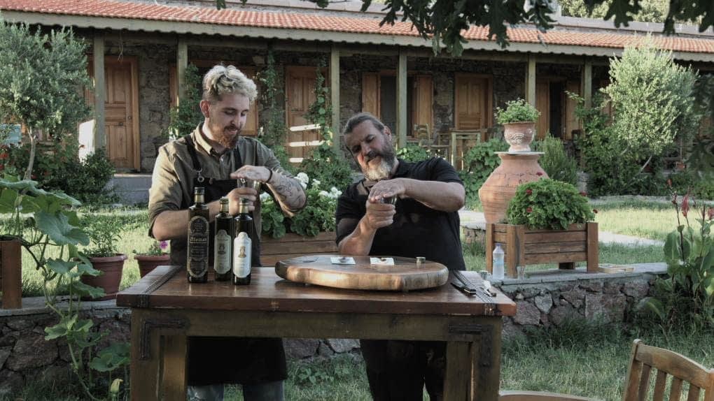 Dvojica muškaraca koji sudjeluju u kušanju maslinovog ulja za drvenim stolom na otvorenom. - Olive Oil Times
