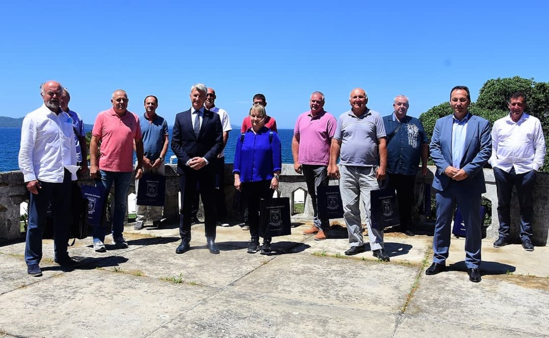 A group of individuals standing together outdoors with a clear blue sky in the background. - Olive Oil Times