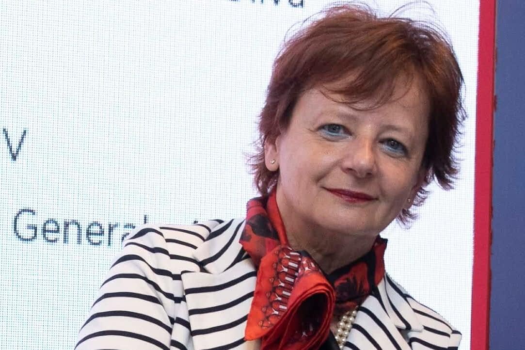 Mujer con cabello corto de color rojo, vestida con un blazer de rayas y una bufanda roja, posando para la cámara. - Olive Oil Times
