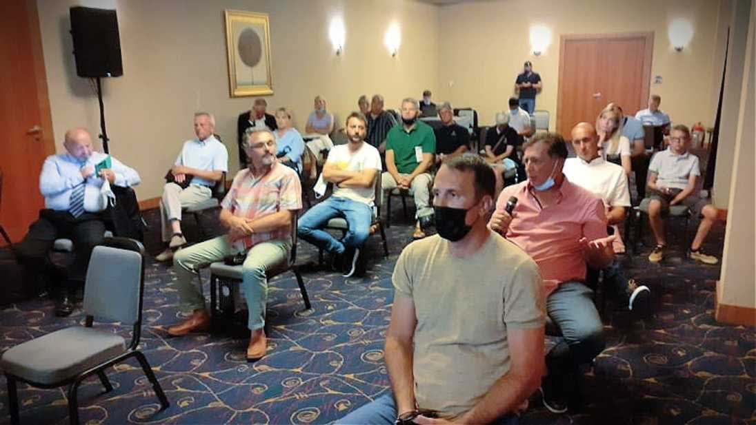 Gruppo di persone sedute in una sala riunioni, alcune delle quali indossano maschere, mentre ascoltano un relatore. Olive Oil Times