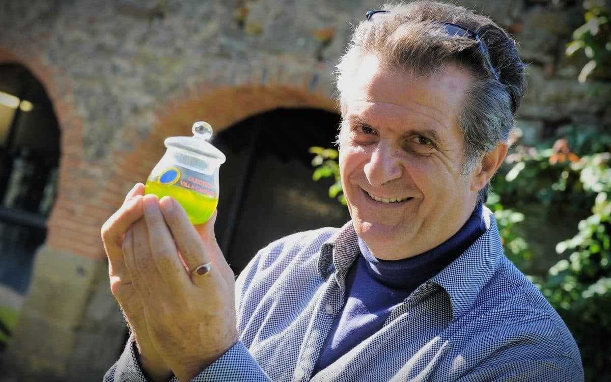 Un homme souriant tout en tenant un petit pot d'huile d'olive verte dans sa main. - Olive Oil Times