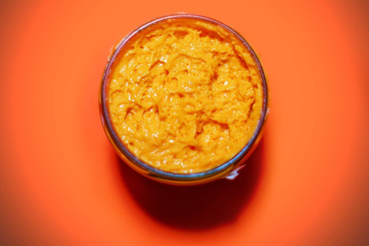 Glass jar filled with orange condiment on a bright orange background. - Olive Oil Times