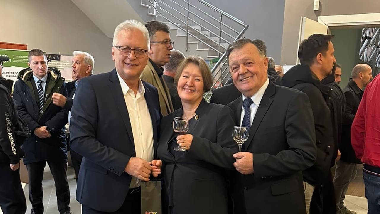 Trois individus debout ensemble, chacun tenant un verre, lors d'un rassemblement ou d'un événement. - Olive Oil Times