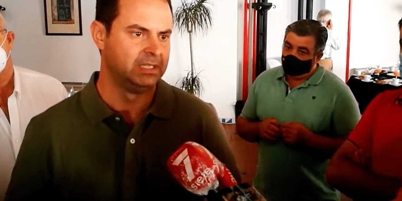 A man in a green shirt speaking to reporters with a microphone in front of him. - Olive Oil Times