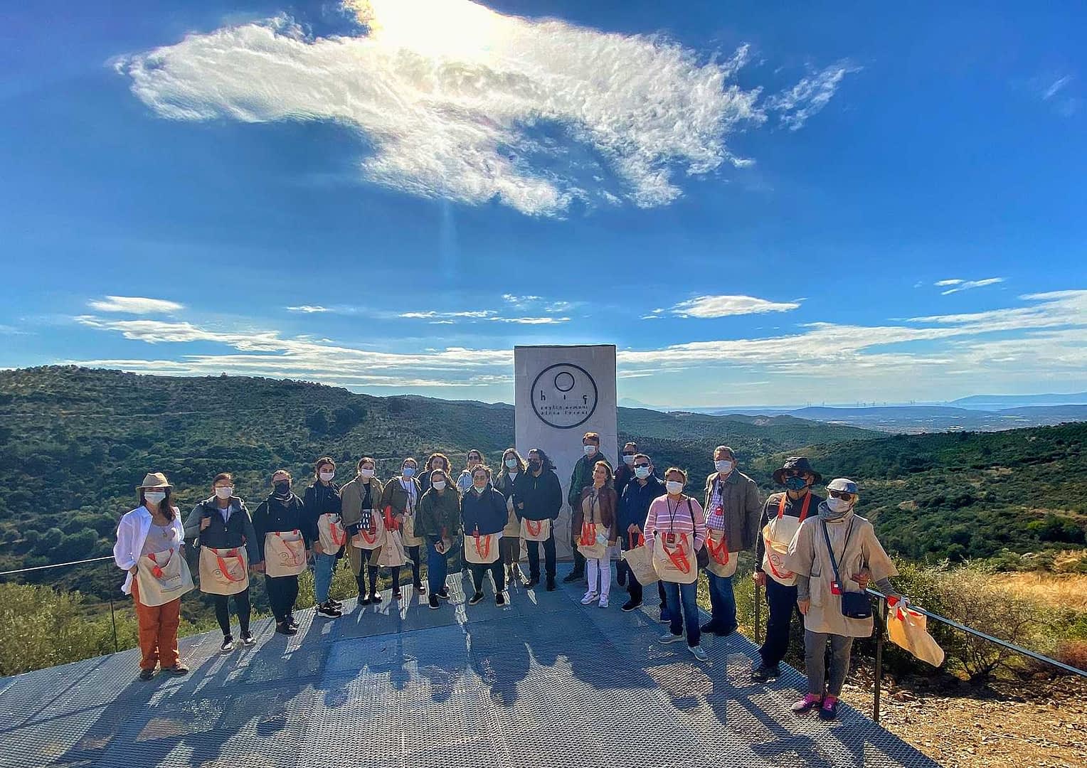 A group of individuals standing together outdoors, wearing bags and posing for a photo in a natural setting. - Olive Oil Times