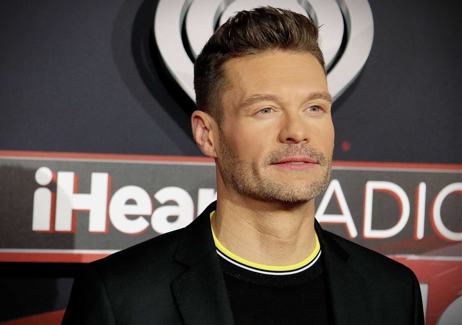 Man wearing a black suit with a yellow collar at an iHeartRadio event red carpet. - Olive Oil Times