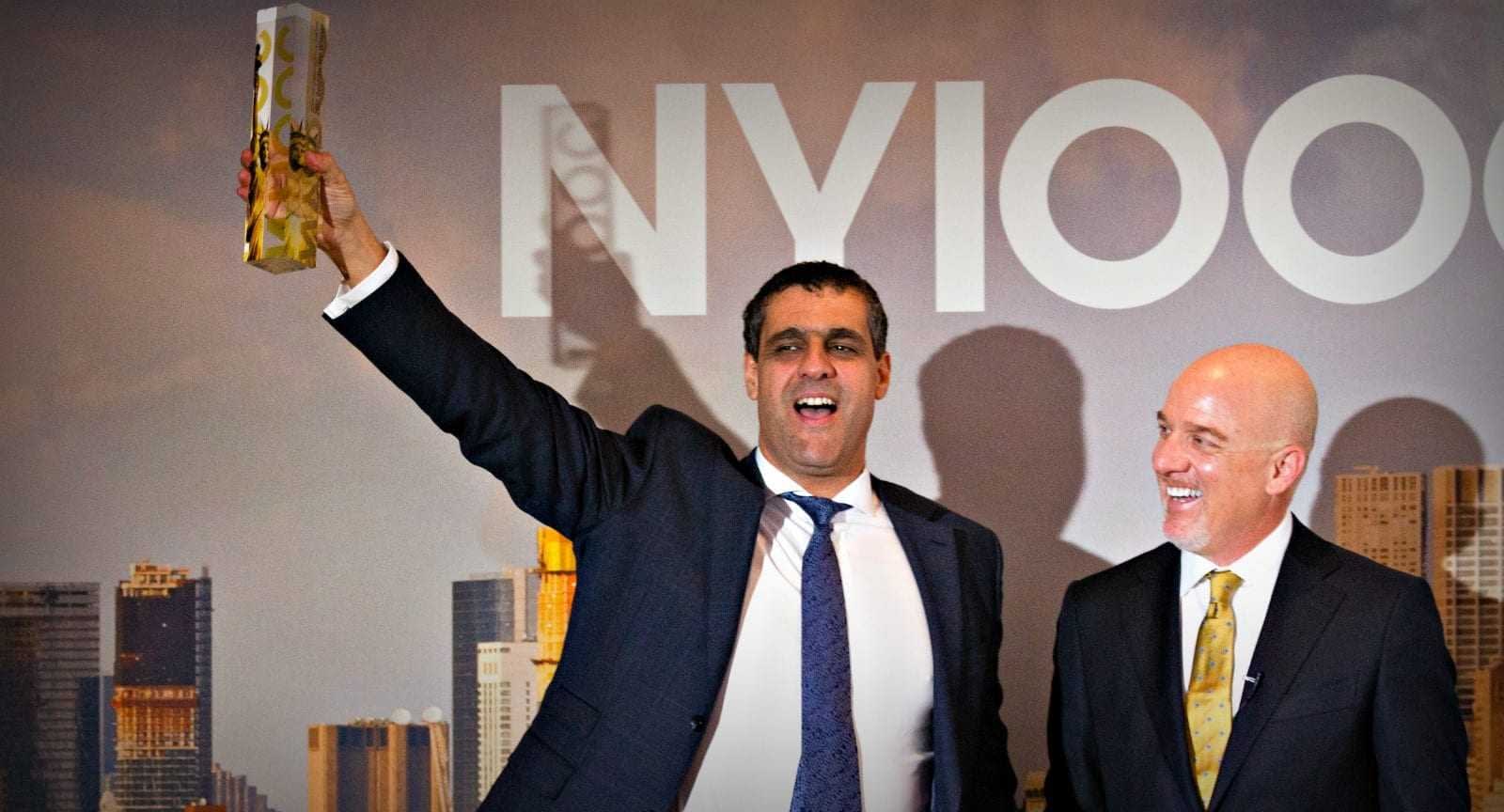 A man in a suit holding an award while standing next to another man in formal attire at an event. - Olive Oil Times