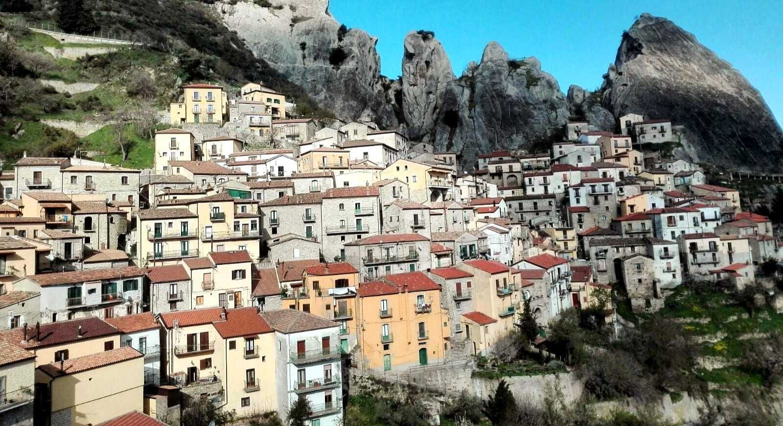 A hillside village featuring colorful houses with red roofs against rocky mountains. - Olive Oil Times