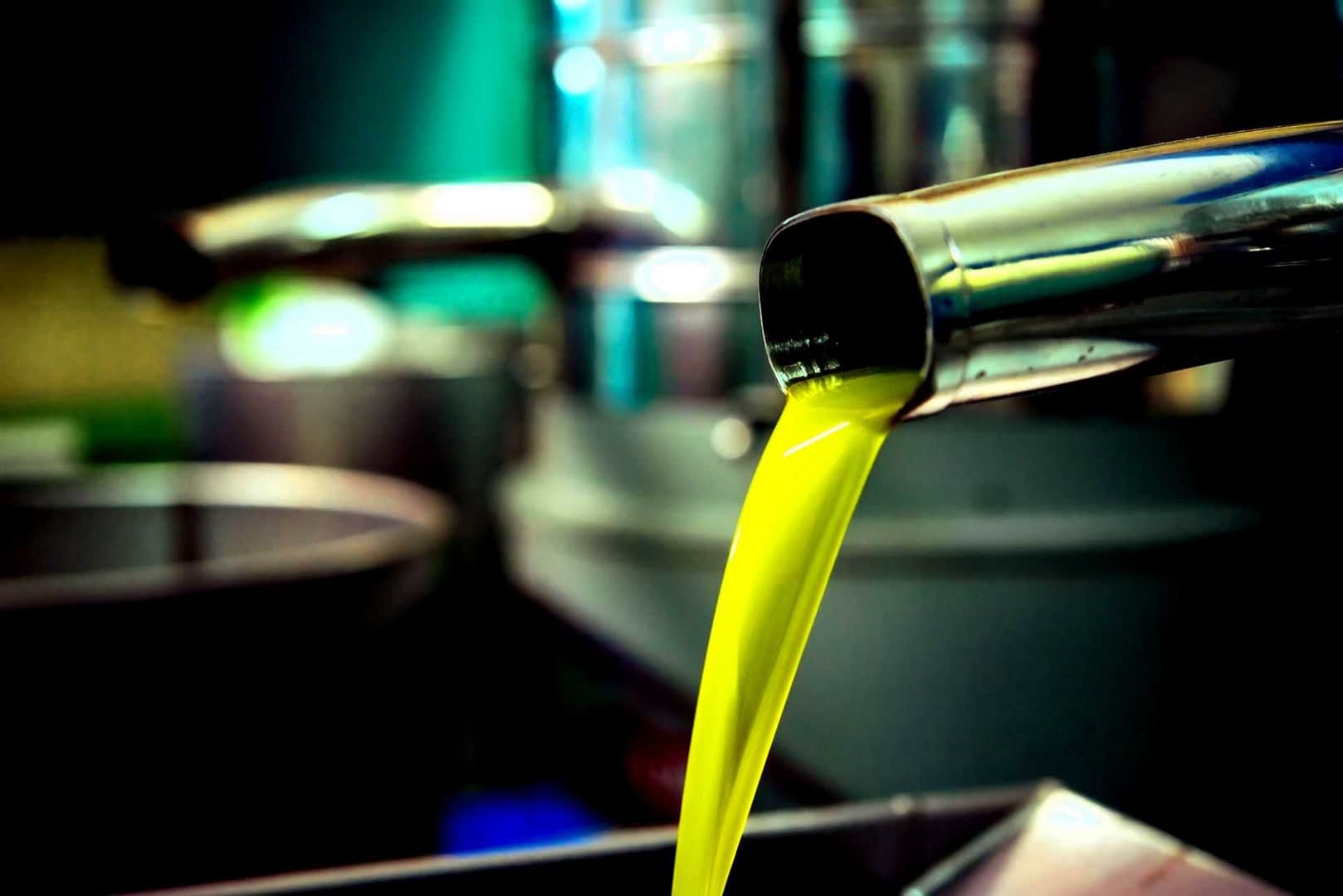 Stream of bright green olive oil pouring from a metal tap into a container. - Olive Oil Times