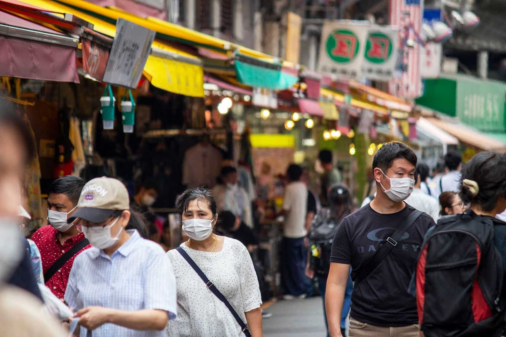 Group of people wearing face masks walking through a market with colorful awnings. - Olive Oil Times
