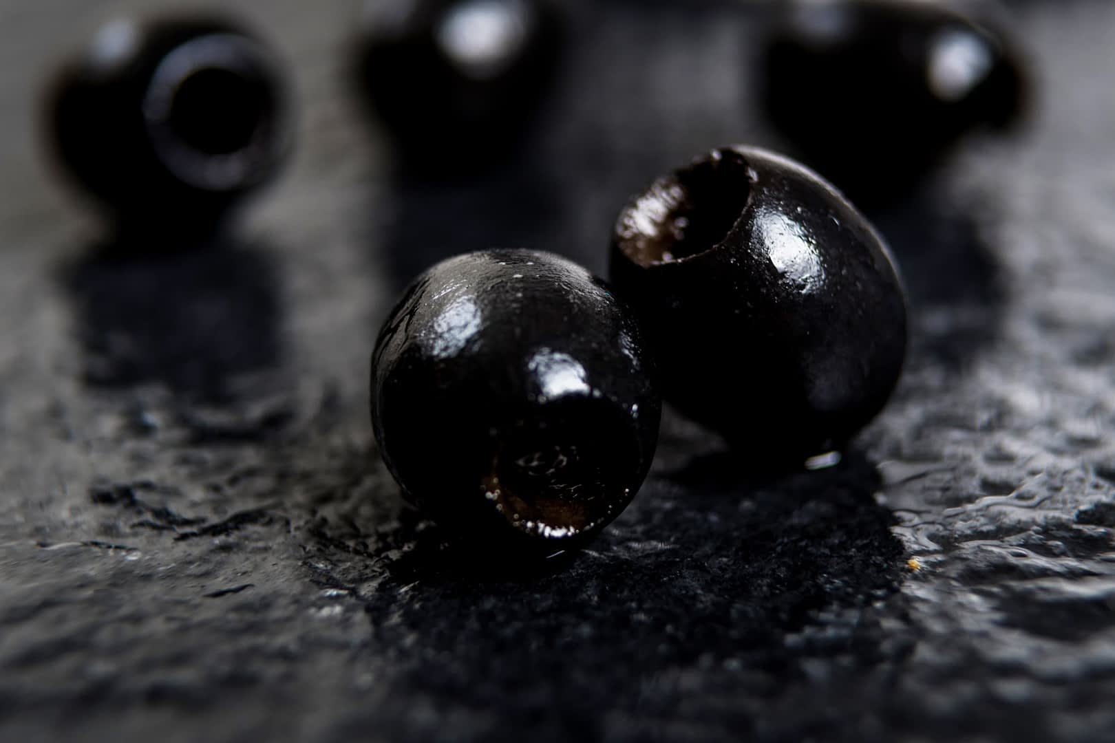 Close-up van zwarte olijven op een donker oppervlak. Olive Oil Times