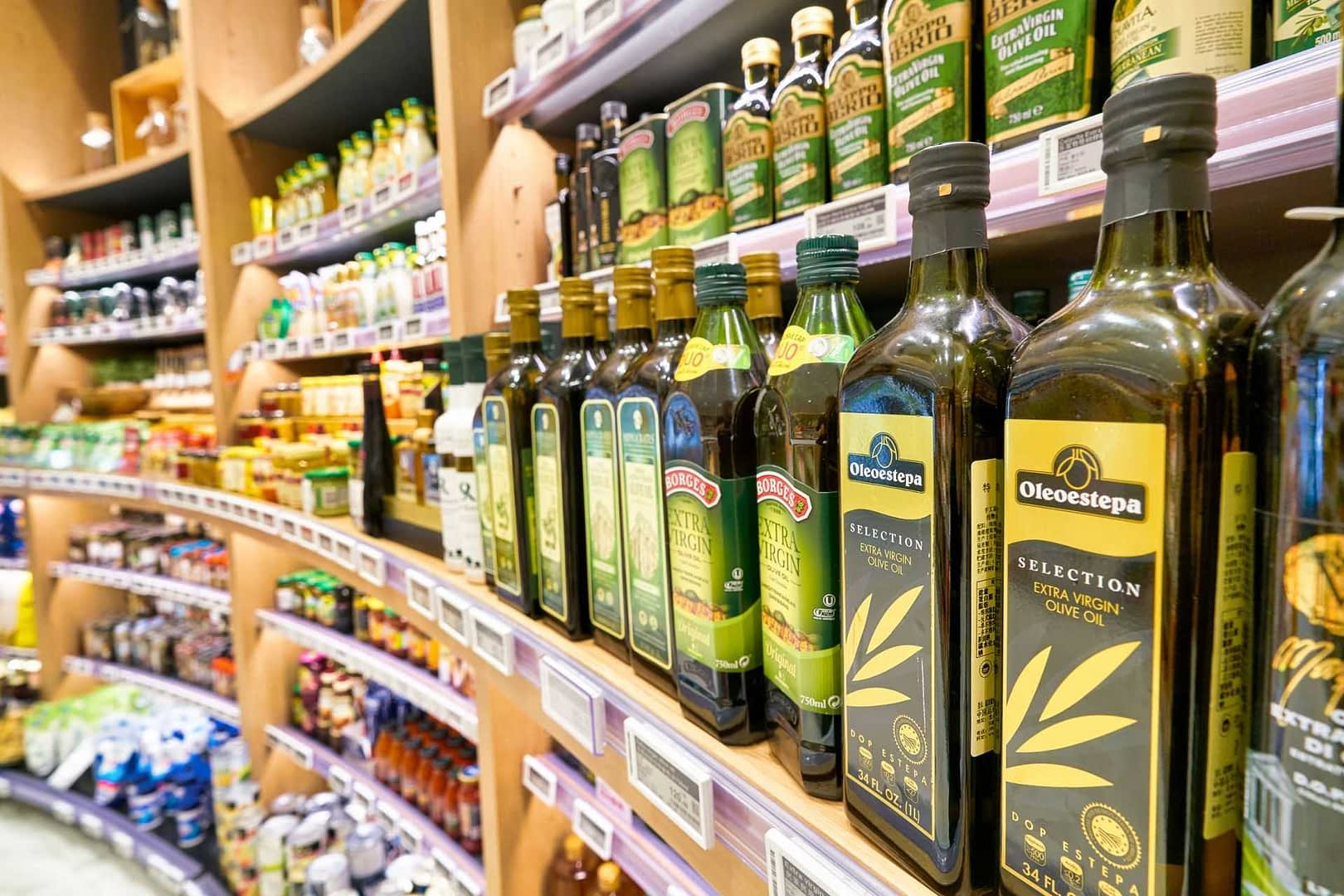 Varias botellas de aceite de oliva expuestas en un estante en una tienda de comestibles. Olive Oil Times