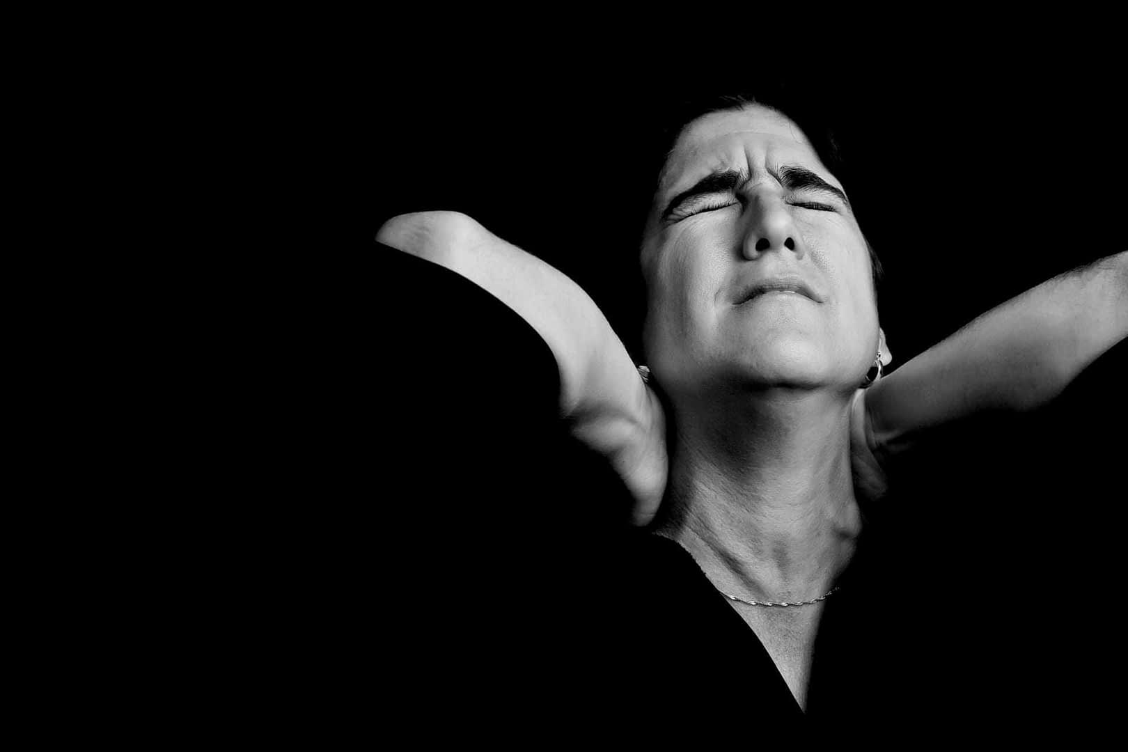 Black and white portrait of a woman with closed eyes and hands on her neck, expressing a moment of contemplation. - Olive Oil Times