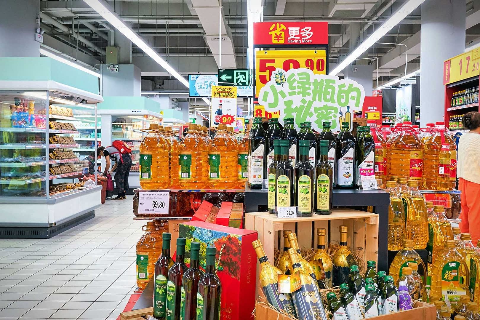 Shelves filled with different brands of cooking oils in a supermarket aisle. - Olive Oil Times