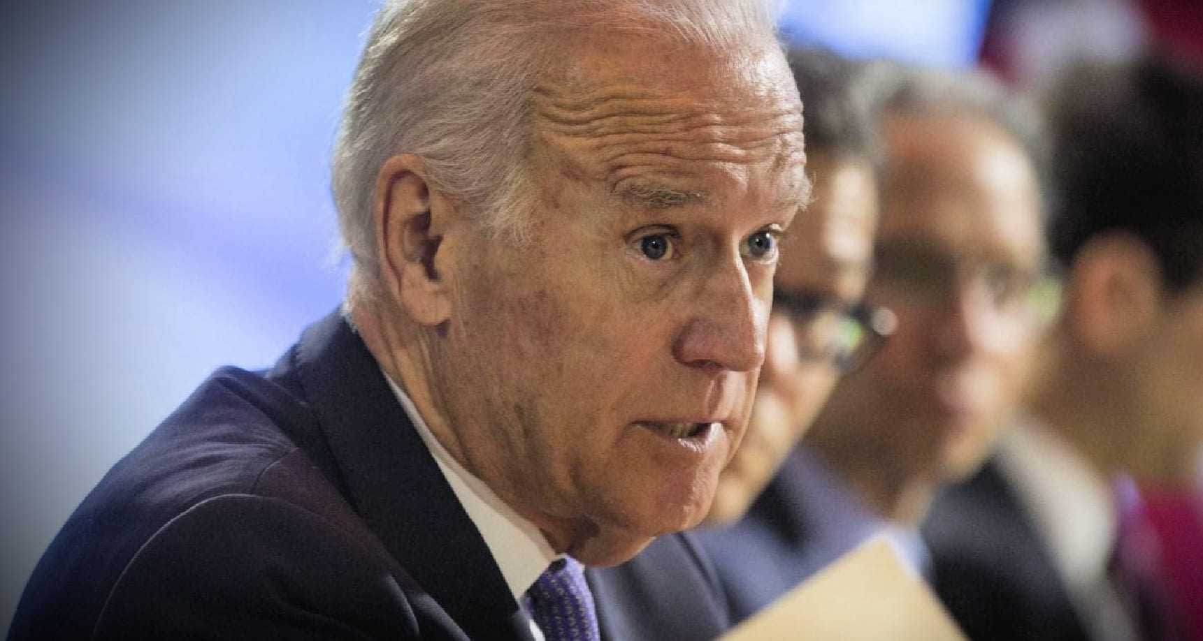 A man in a suit speaking during a conference, holding a document in his hand. - Olive Oil Times