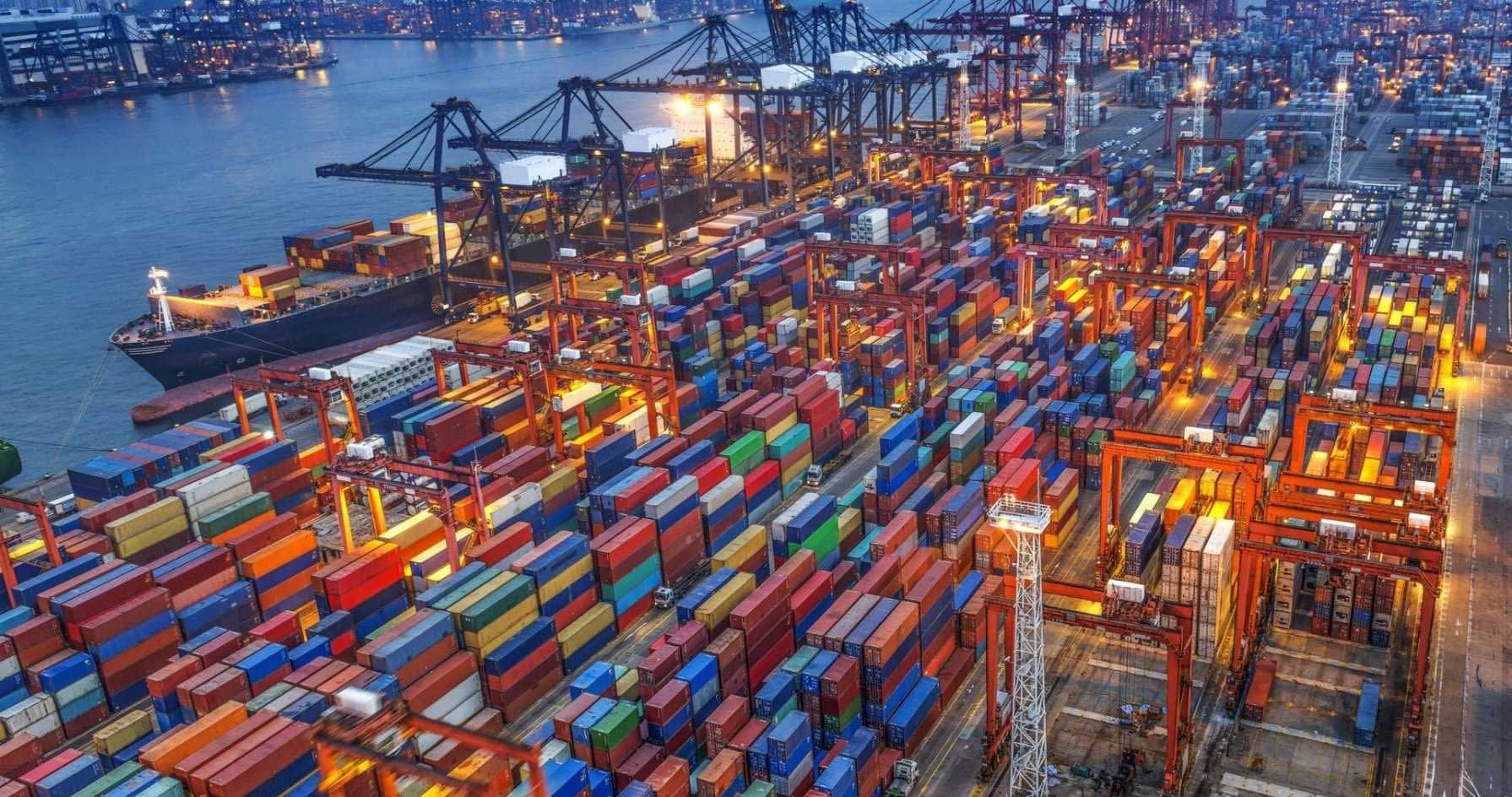 Aerial view of a shipping port filled with colorful containers and cranes at night. - Olive Oil Times