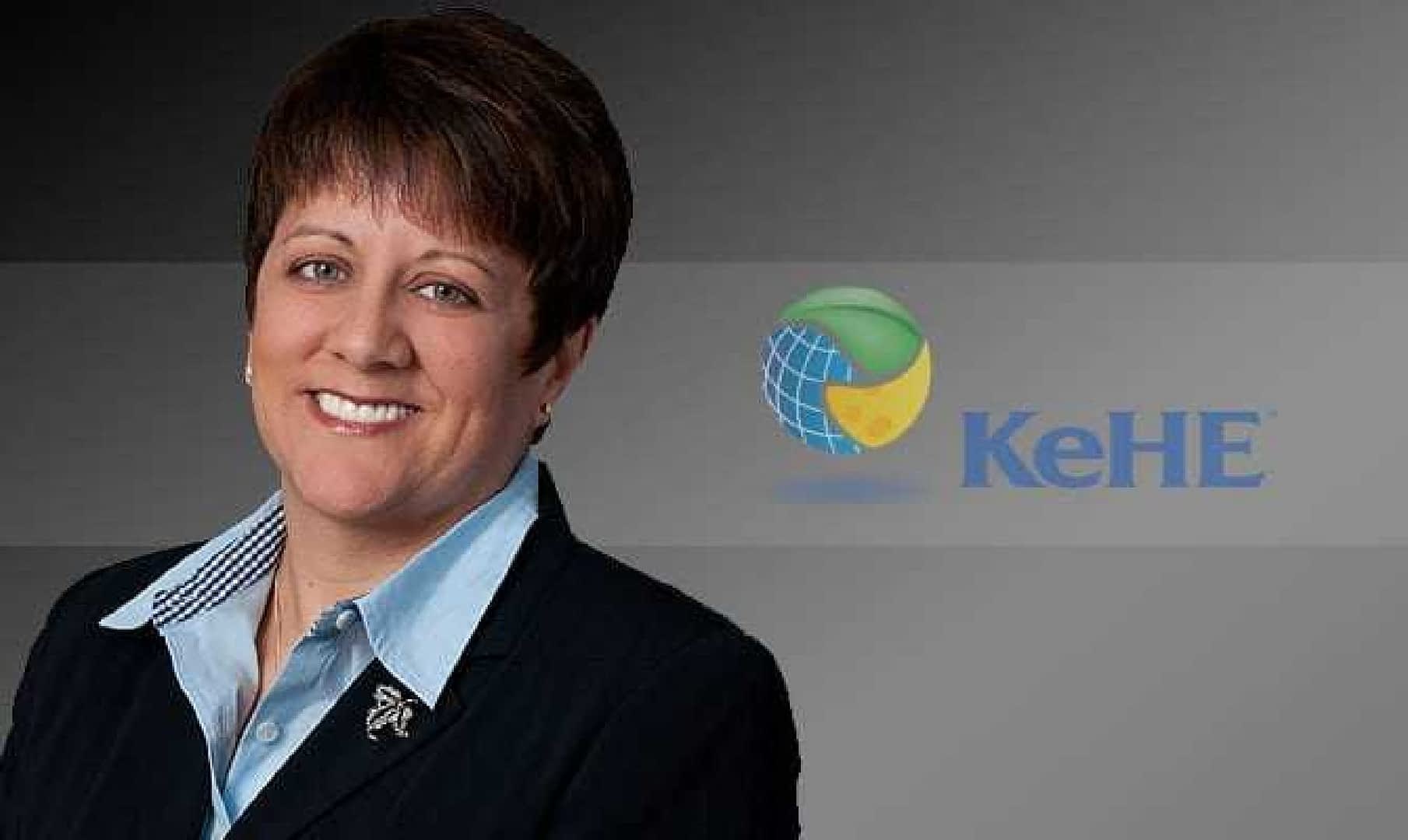 A business executive in a black suit with a light blue shirt, smiling against a dark background with the KeHE logo. - Olive Oil Times