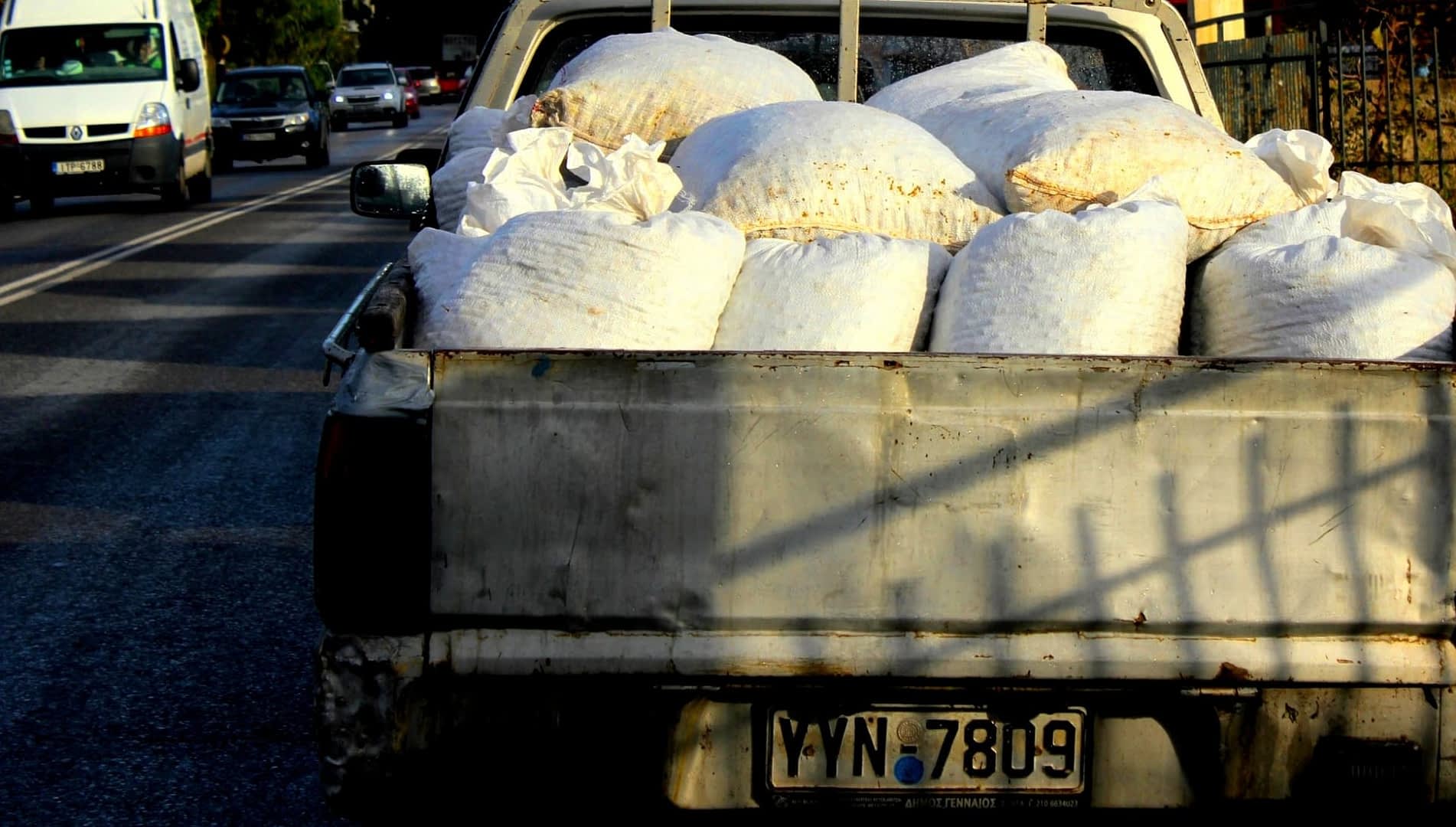 Pickup truck with a bed full of white bags on a street. - Olive Oil Times