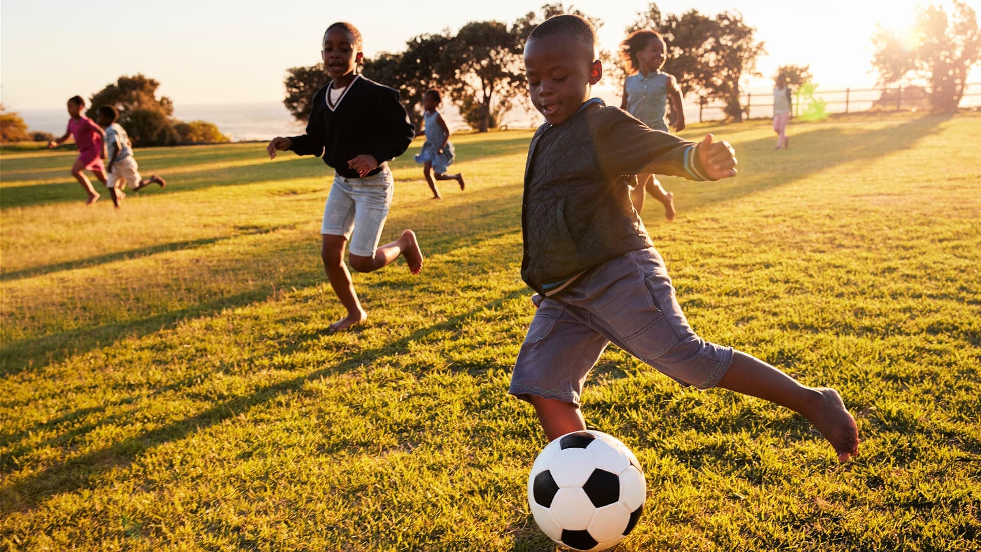Eine Gruppe von Kindern rennt und spielt Fußball auf einer Wiese während des Sonnenuntergangs. - Olive Oil Times