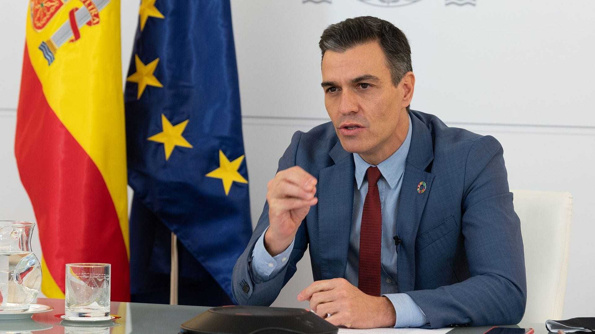 Un hombre con traje azul habla durante una conferencia con banderas de España y la Unión Europea de fondo. - Olive Oil Times