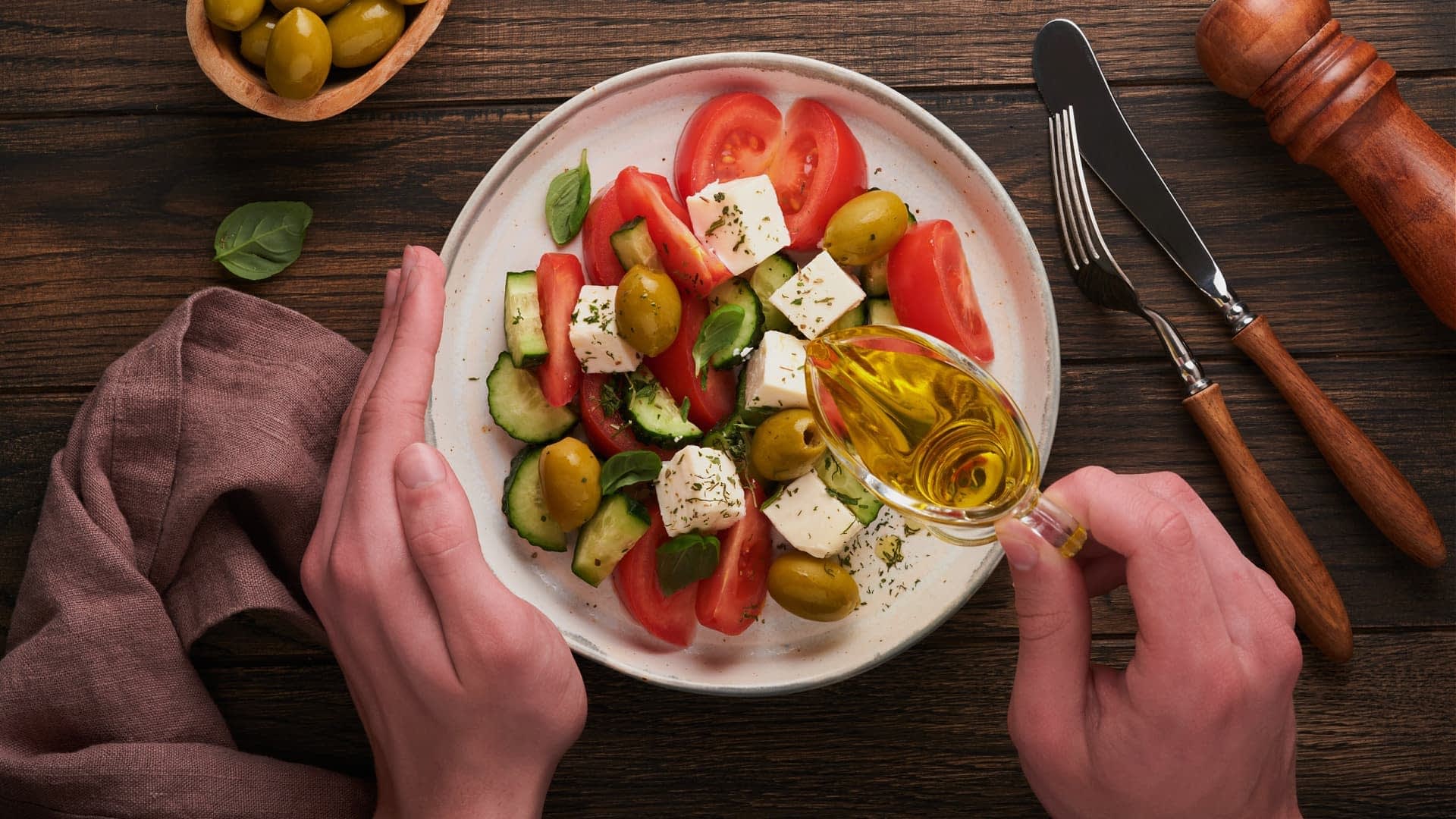 将橄榄油倒在盘子里的西红柿、黄瓜、橄榄和羊乳酪沙拉上。 - Olive Oil Times