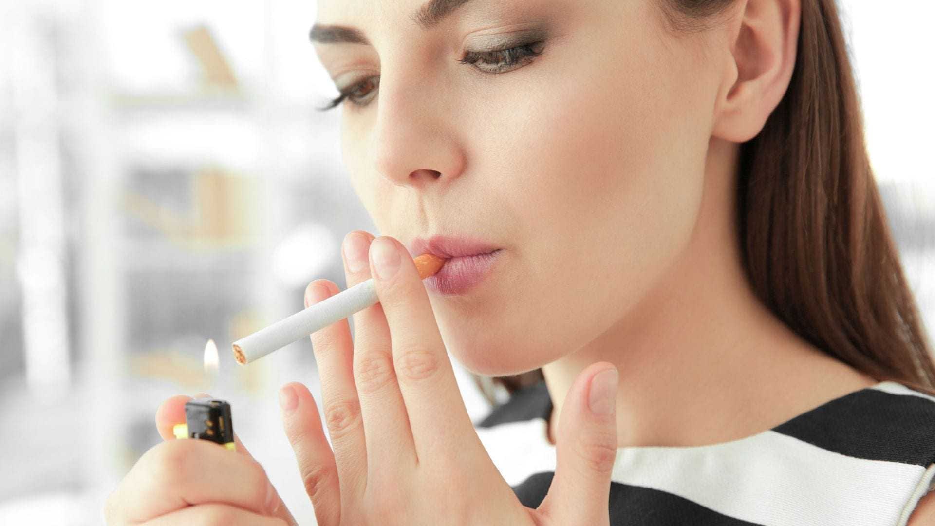 A woman with long hair lighting a cigarette with a lighter in her hand. - Olive Oil Times