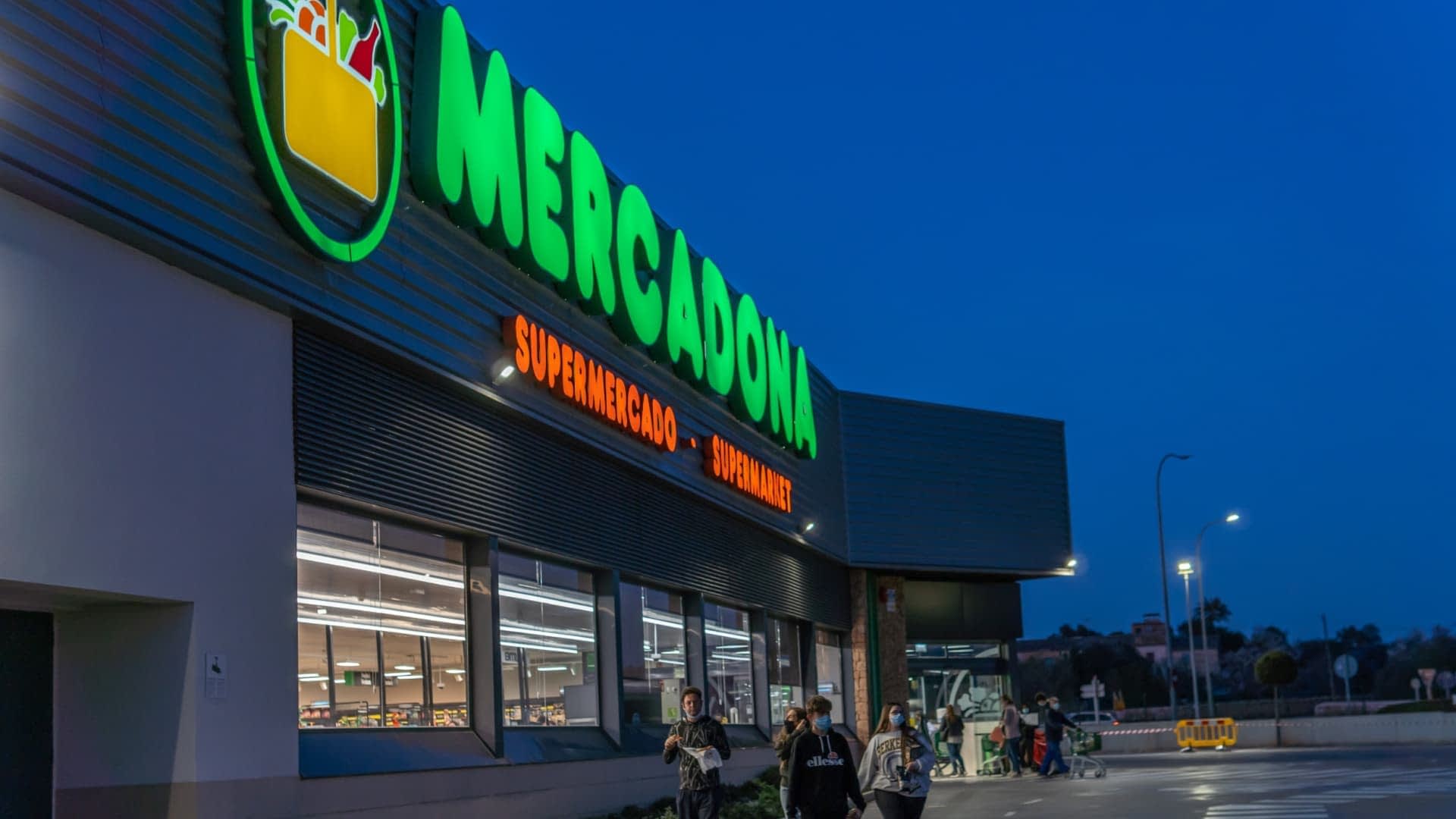 Buitenaanzicht van een Mercadona-supermarkt met verlichte reclameborden tijdens de schemering. Olive Oil Times