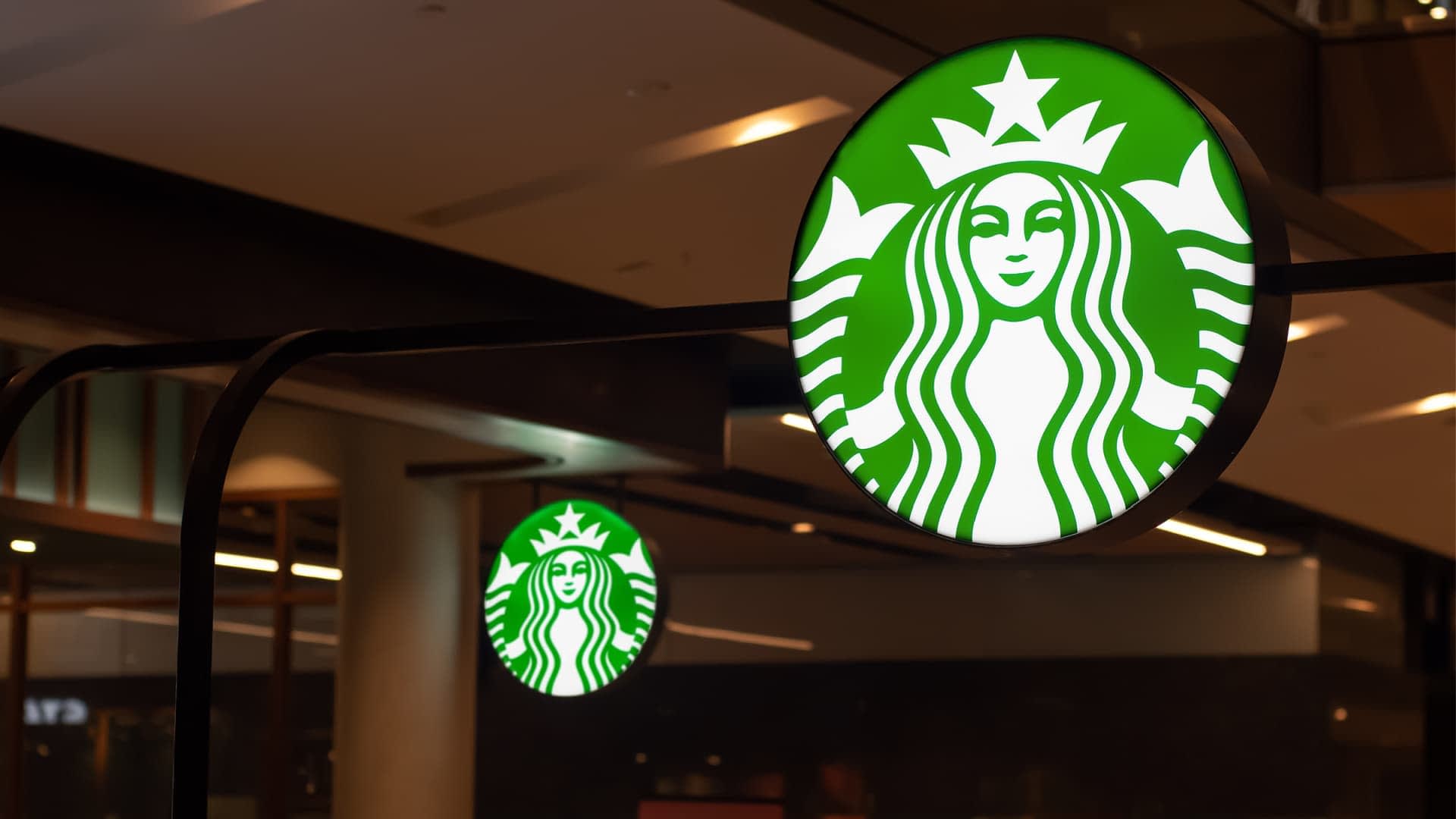 Beleuchtetes Starbucks-Logoschild mit grünem Hintergrund und weißem Meerjungfrauen-Design. – Olive Oil Times