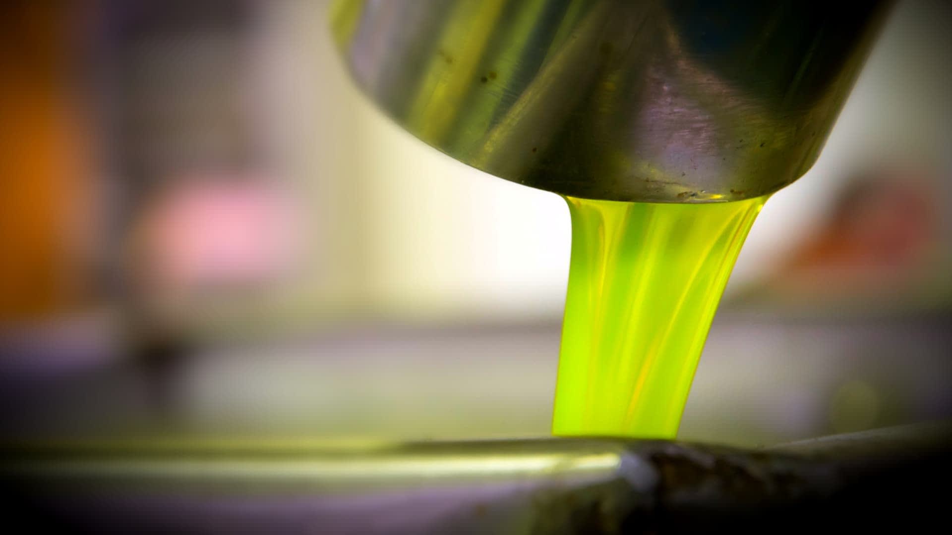 Aceite de oliva de color verde brillante que se vierte desde un recipiente de metal a un tazón. - Olive Oil Times