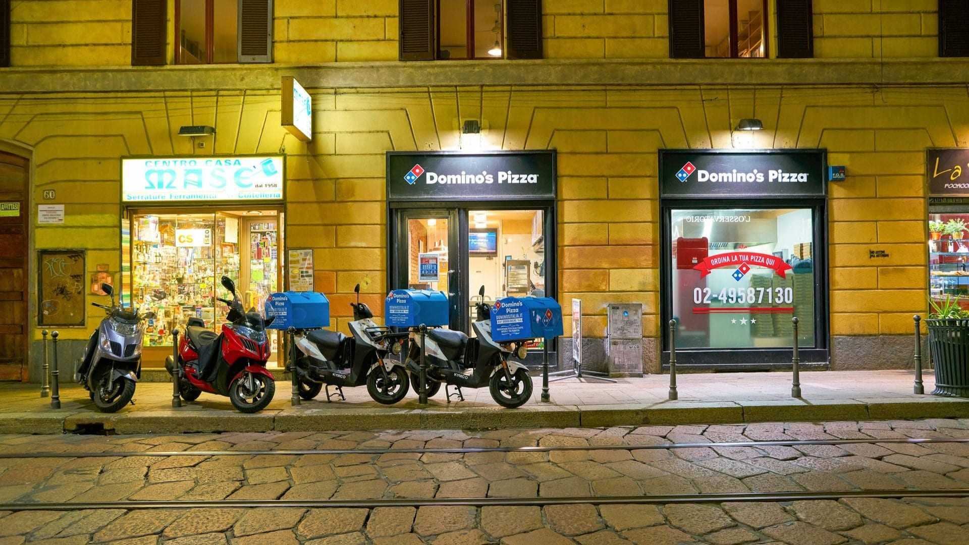 Vrsta dostavnih motorjev, parkiranih pred lokacijo Domino's Pizza ponoči. - Olive Oil Times