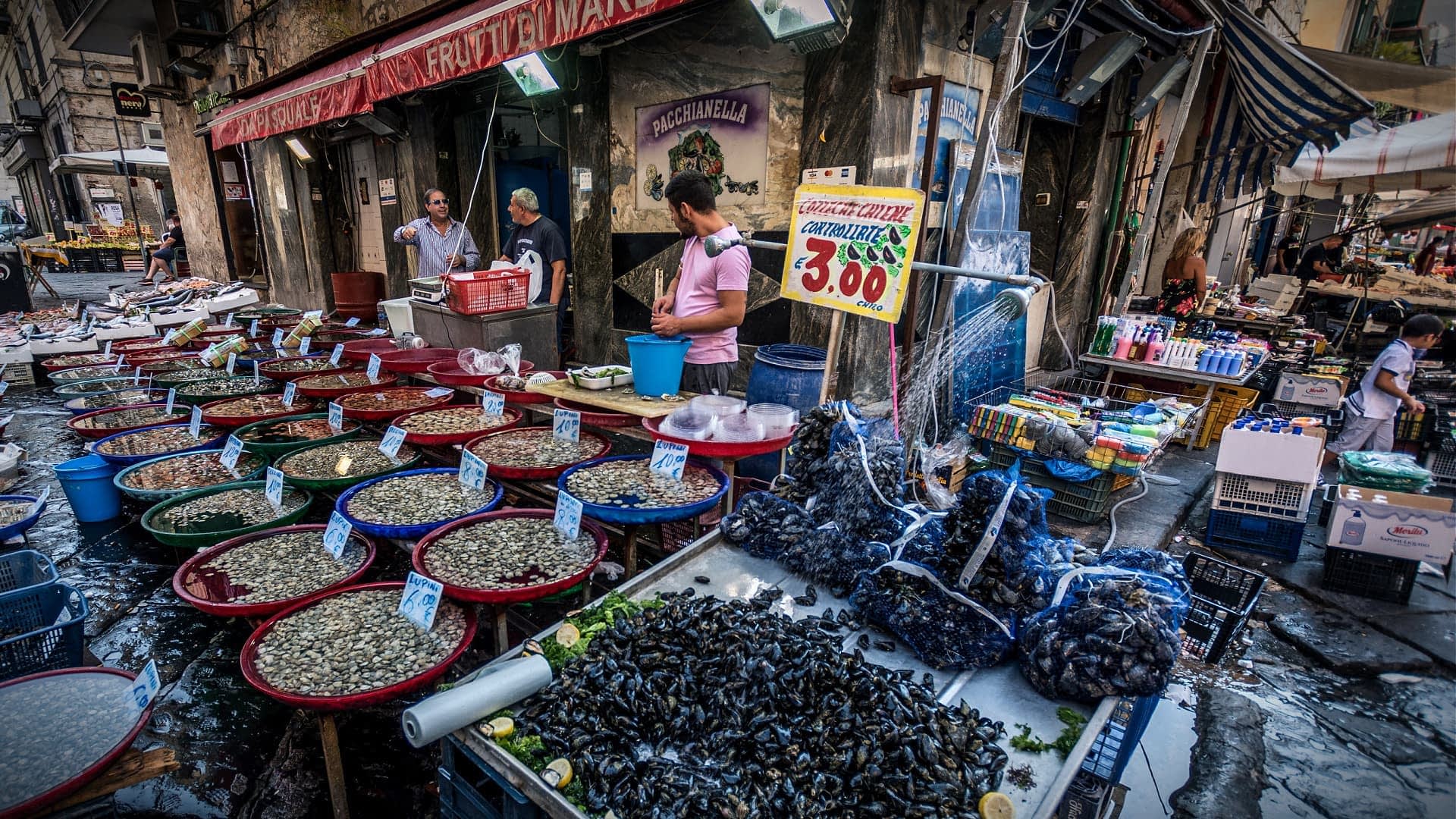 Un mercado de mariscos que exhibe varios tipos de mariscos y pescados en recipientes coloridos. Olive Oil Times