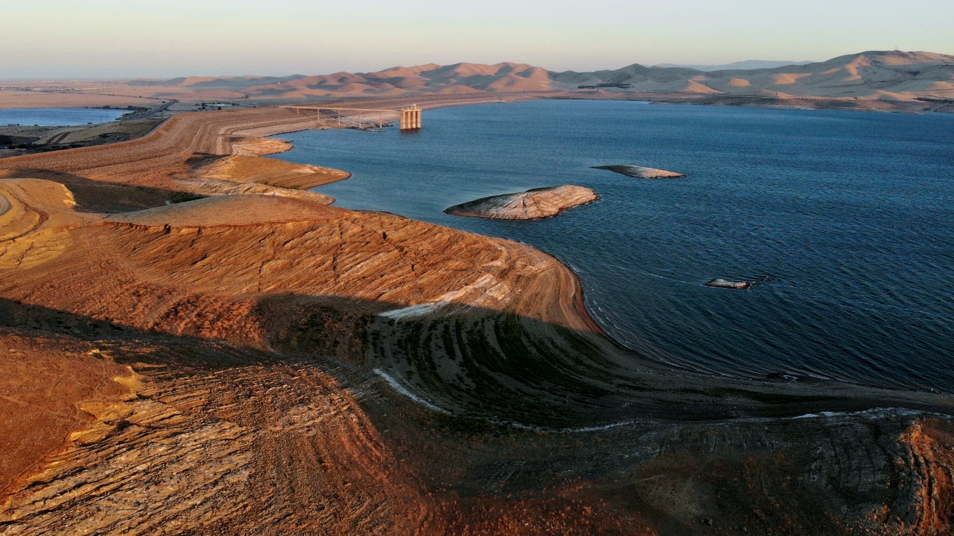 Vista aérea de um reservatório com terra seca e colinas ao fundo durante o pôr do sol. - Olive Oil Times