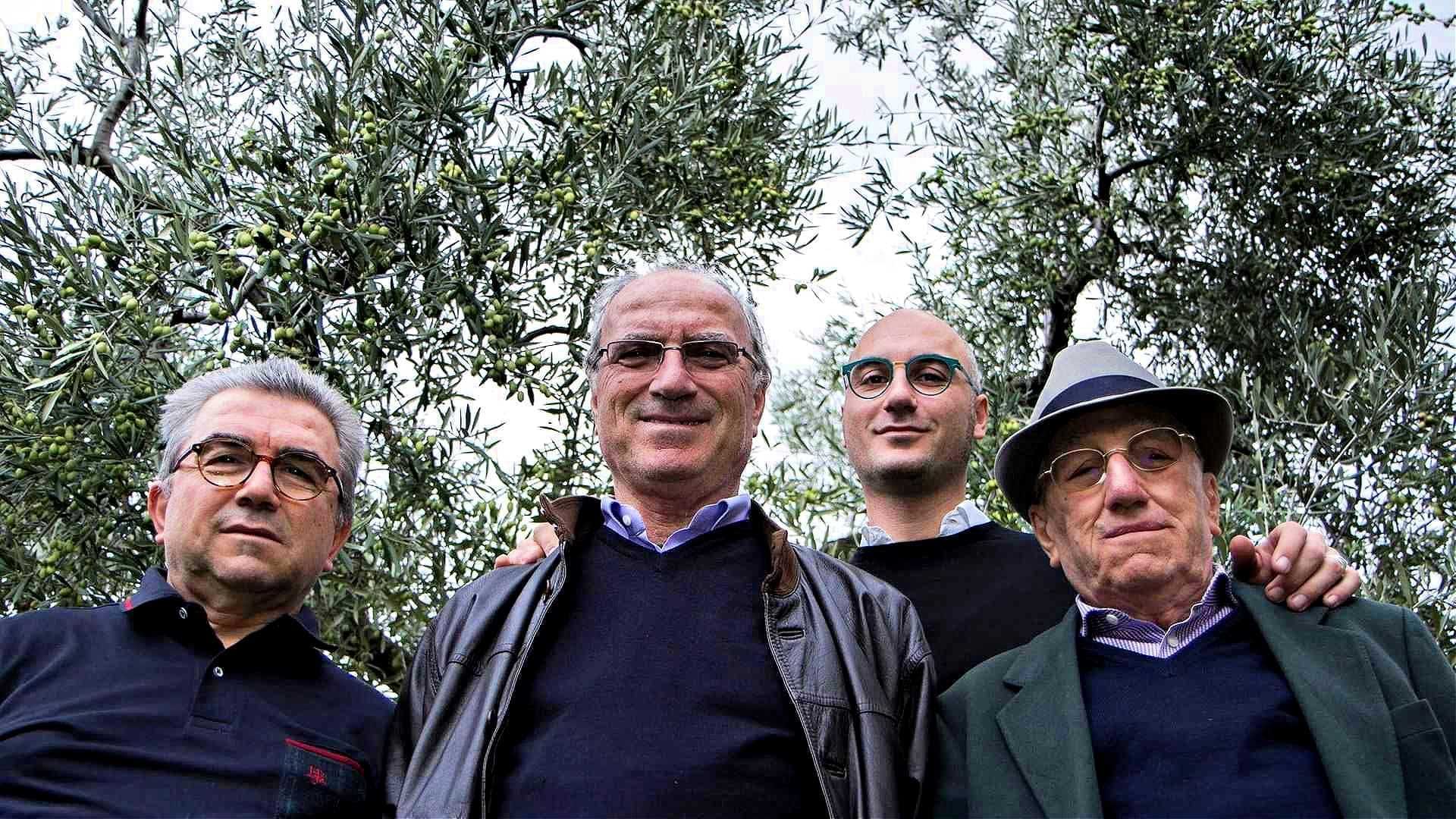 Quatro homens juntos ao ar livre entre oliveiras, todos olhando para a câmera. - Olive Oil Times