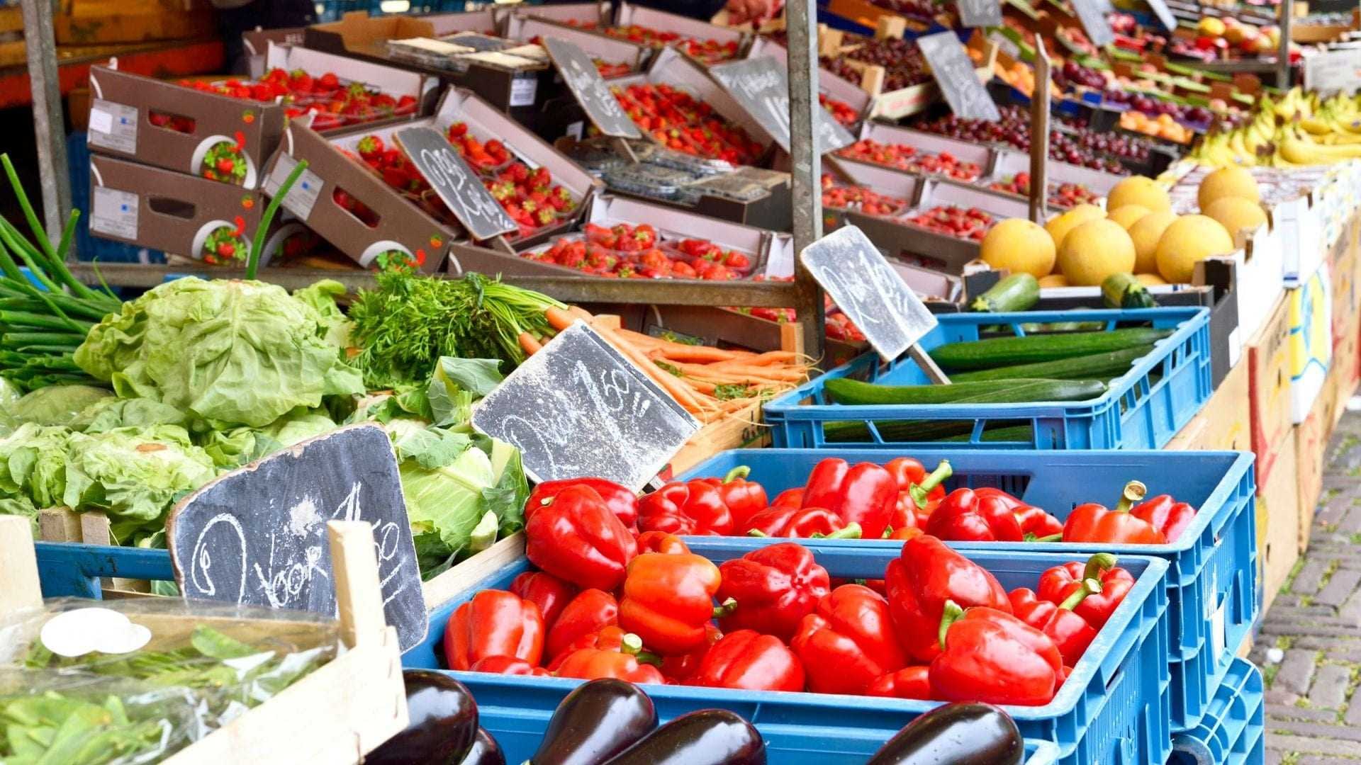 Šareni asortiman svježeg povrća i voća složenog u sanduke na tržnici. - Olive Oil Times