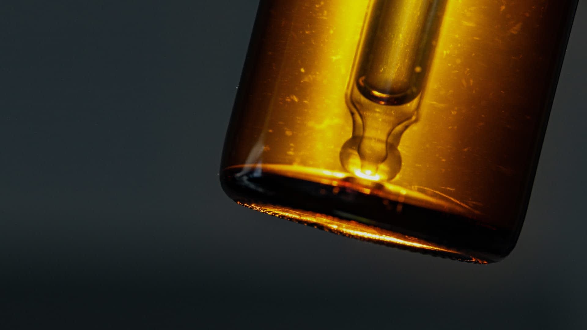 Gros plan d'un flacon compte-gouttes en verre ambré avec un bouchon pipette sur un fond sombre. - Olive Oil Times