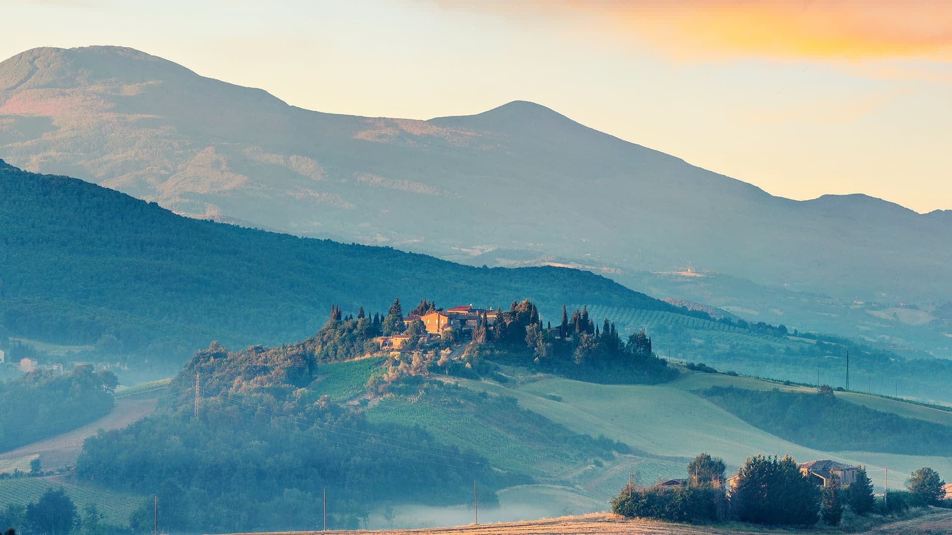 Een schilderachtig uitzicht op het Toscaanse landschap met glooiende heuvels en een boerderij op een heuveltop. Olive Oil Times