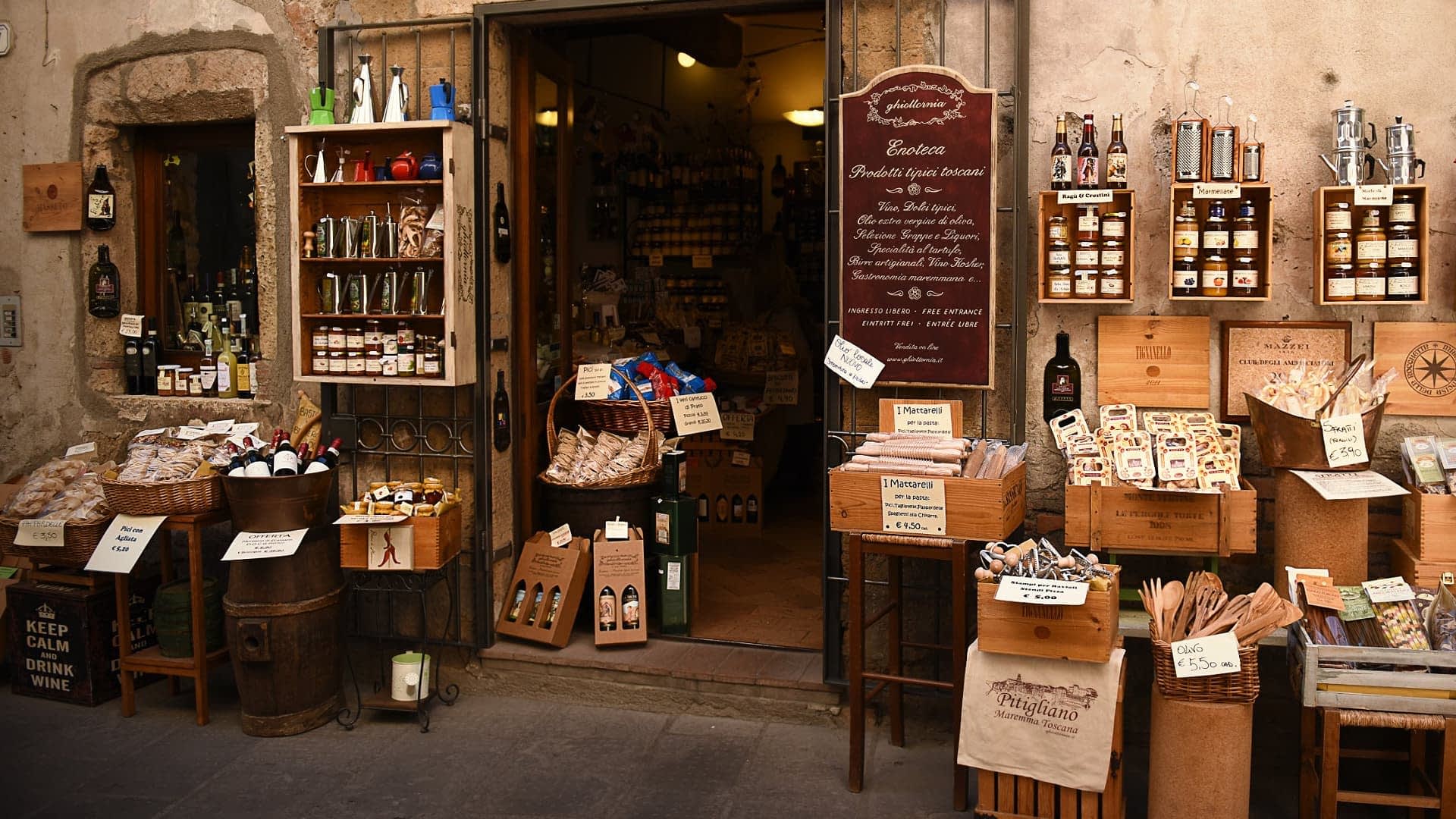 Entrada de uma loja de alimentos especializados em comida italiana com vários produtos expostos do lado de fora. - Olive Oil Times