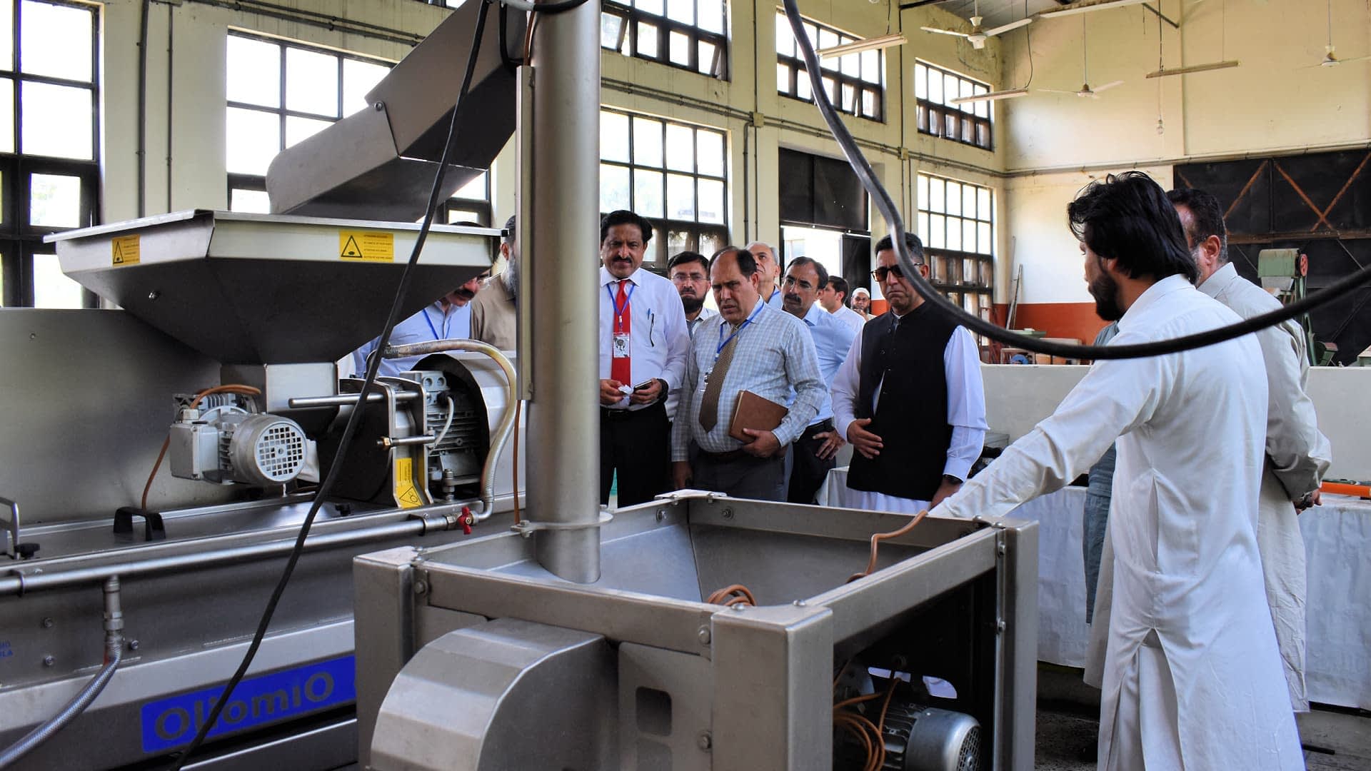 Grupo de personas observando una máquina de extracción de aceite durante una demostración en un entorno industrial. Olive Oil Times