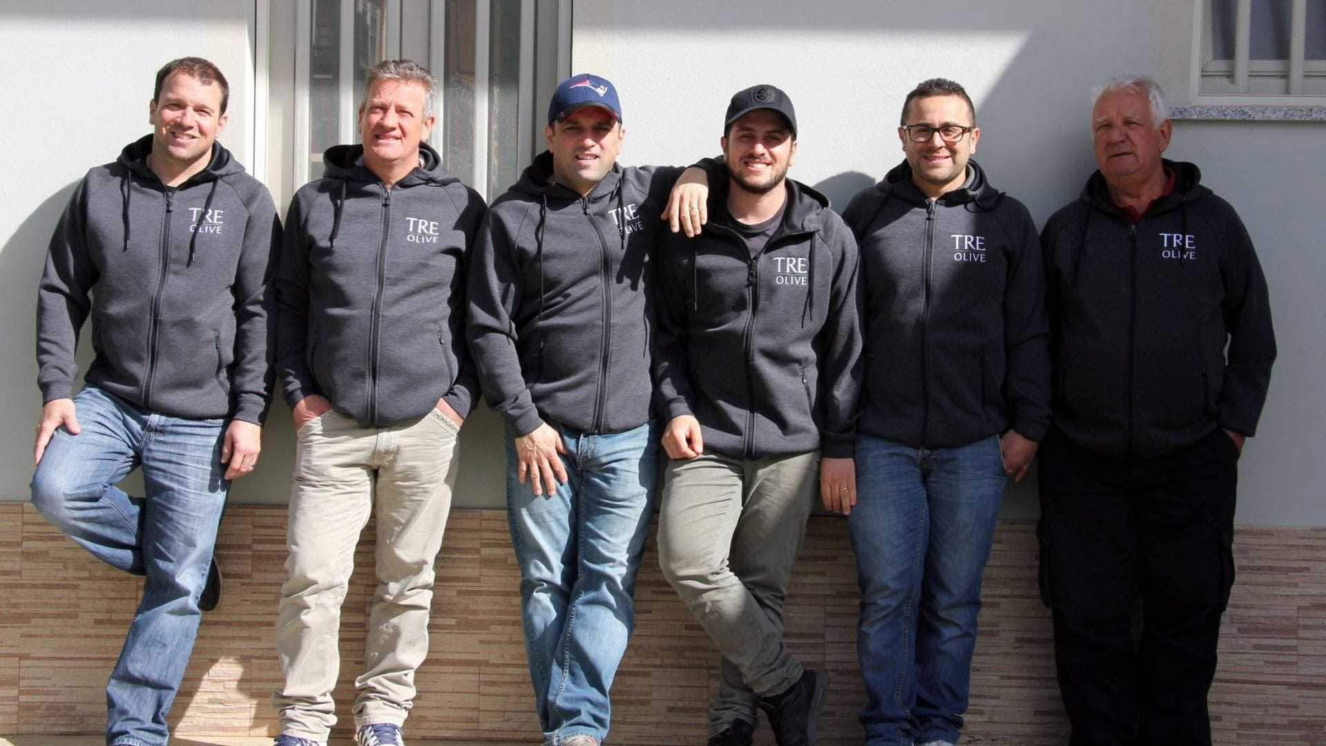 Six men standing in a row wearing gray hoodies with 'TRE Olive' printed on them. - Olive Oil Times