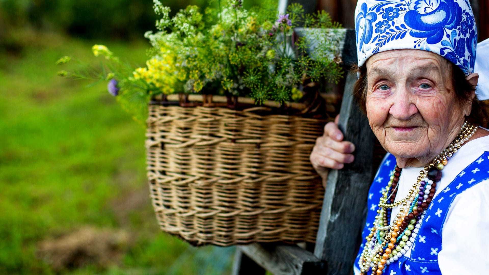 Elderly woman wearing traditional clothing and a headscarf, holding a basket of flowers. - Olive Oil Times