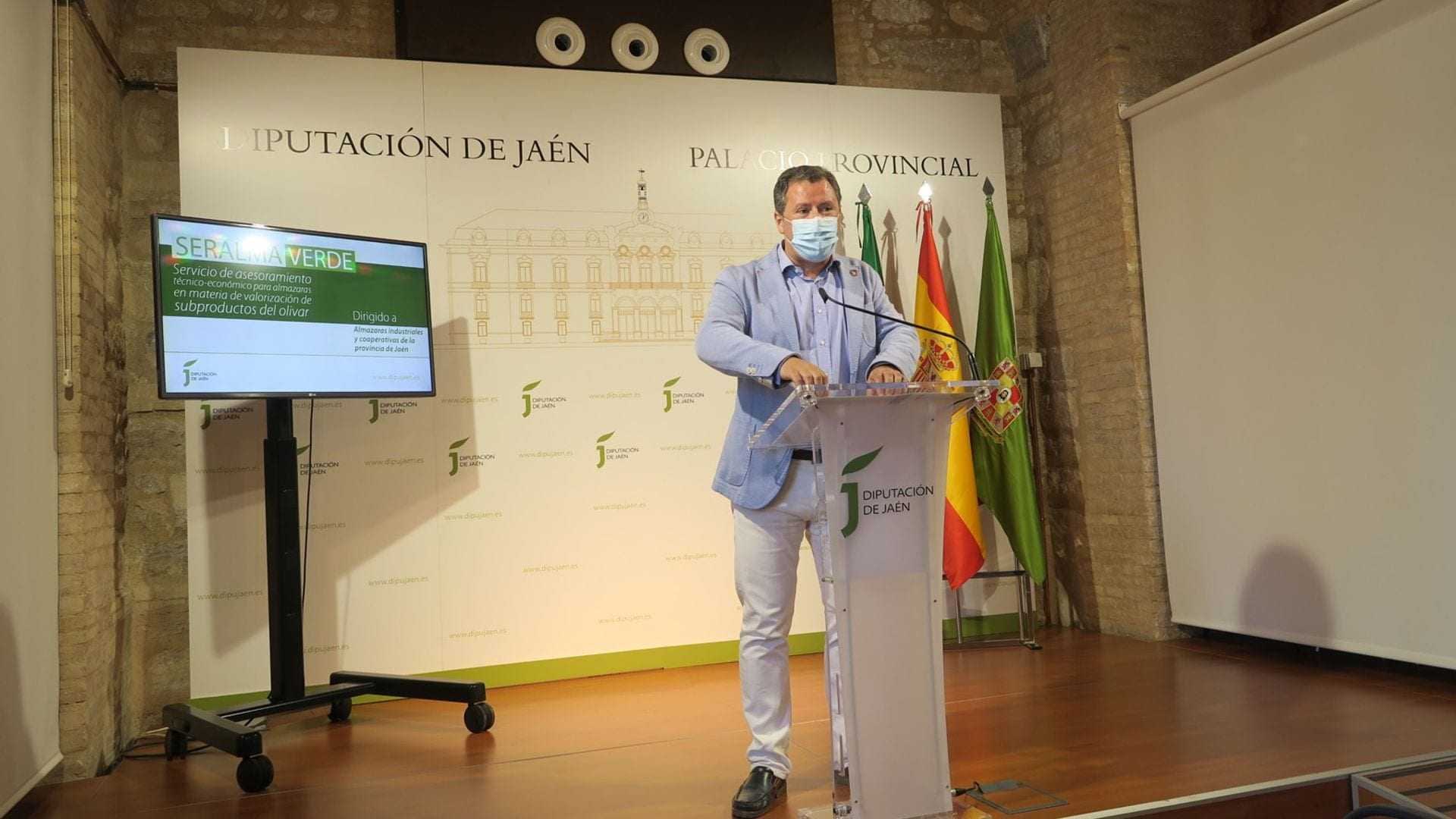 Man speaking at a podium during a press conference at Diputación de Jaén with a screen in the background. - Olive Oil Times