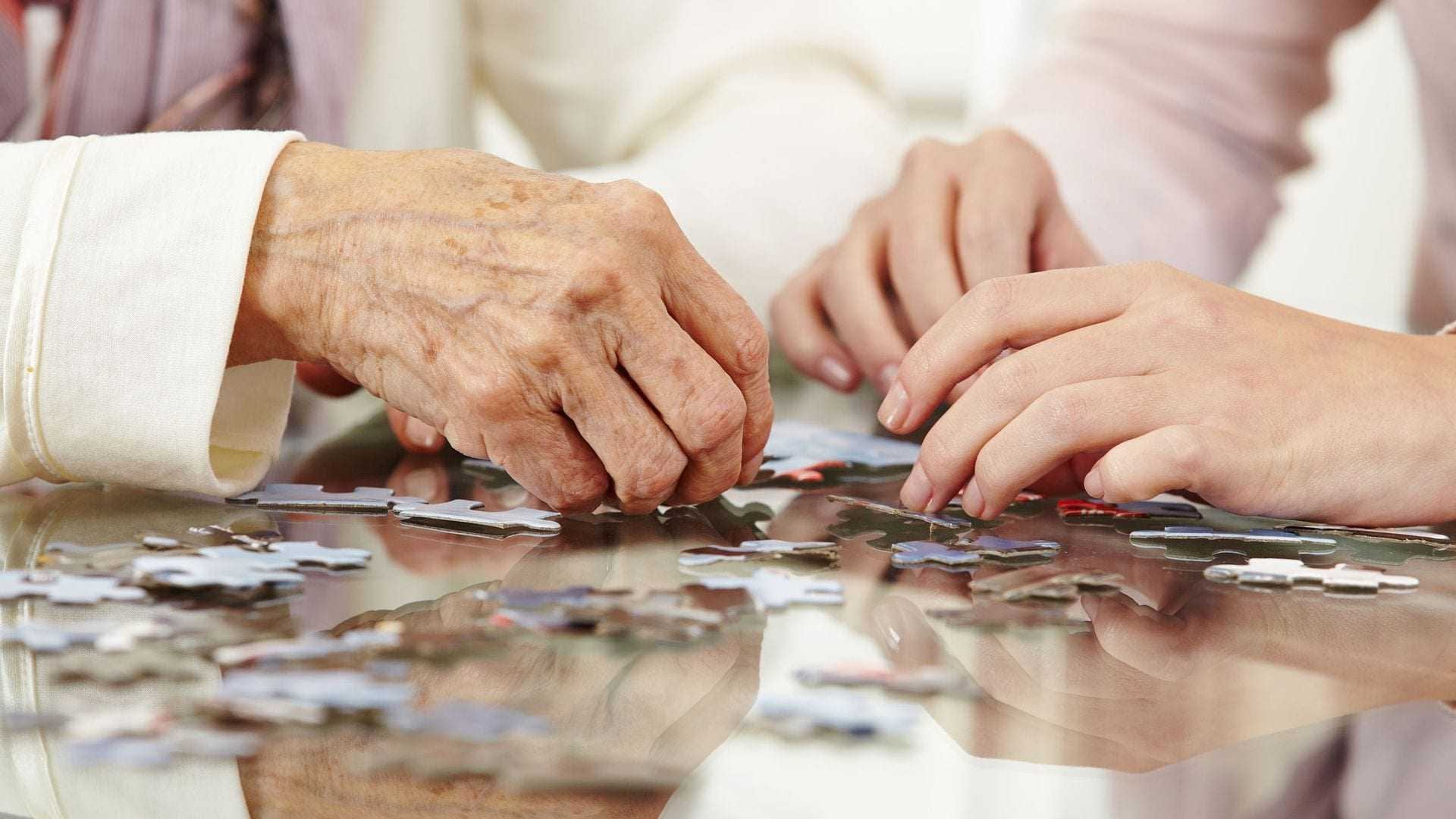 Two hands working together to assemble pieces of a jigsaw puzzle on a table. - Olive Oil Times