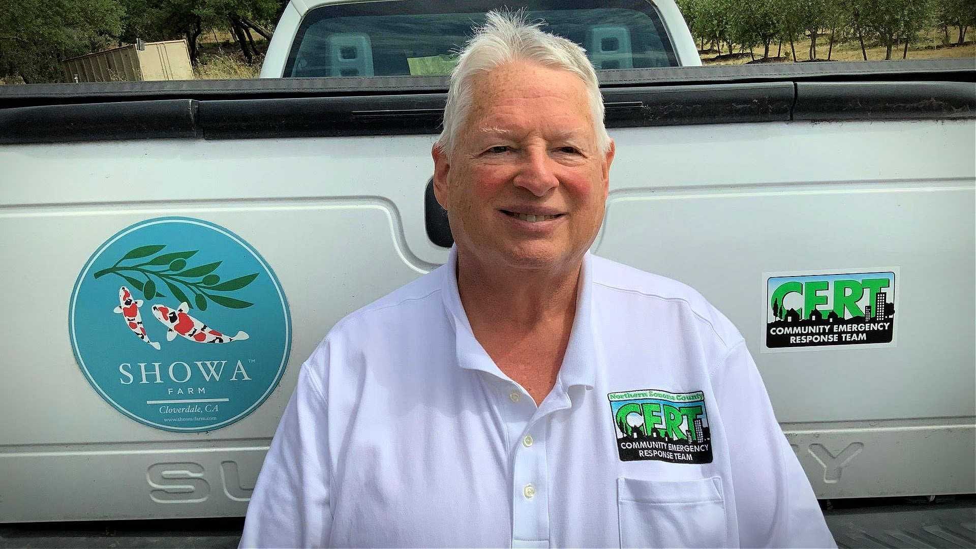 Man wearing a white shirt with a Community Emergency Response Team badge standing by a truck. - Olive Oil Times