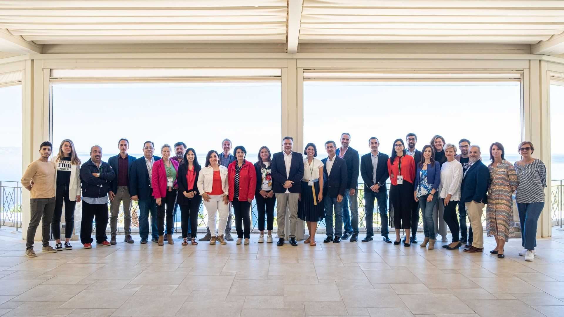 A group of individuals posing for a photo at an event, standing together in a spacious indoor area. - Olive Oil Times