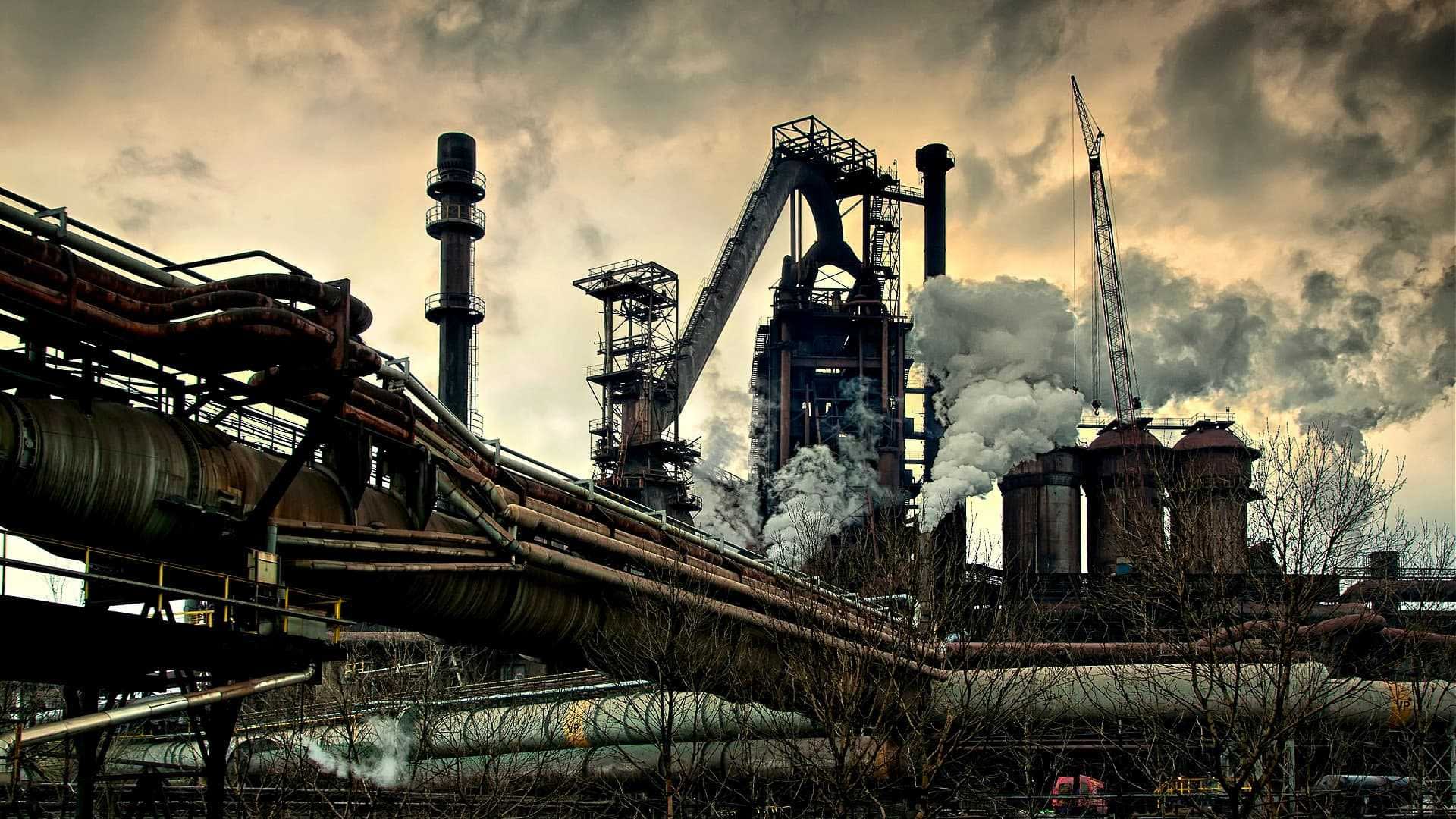 Industrial steel mill featuring large smoke stacks and pipes with visible emissions. - Olive Oil Times