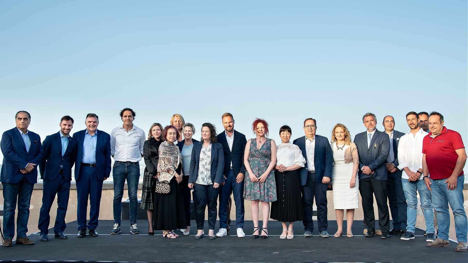 A group of individuals standing together outdoors for a photo against a clear sky. - Olive Oil Times