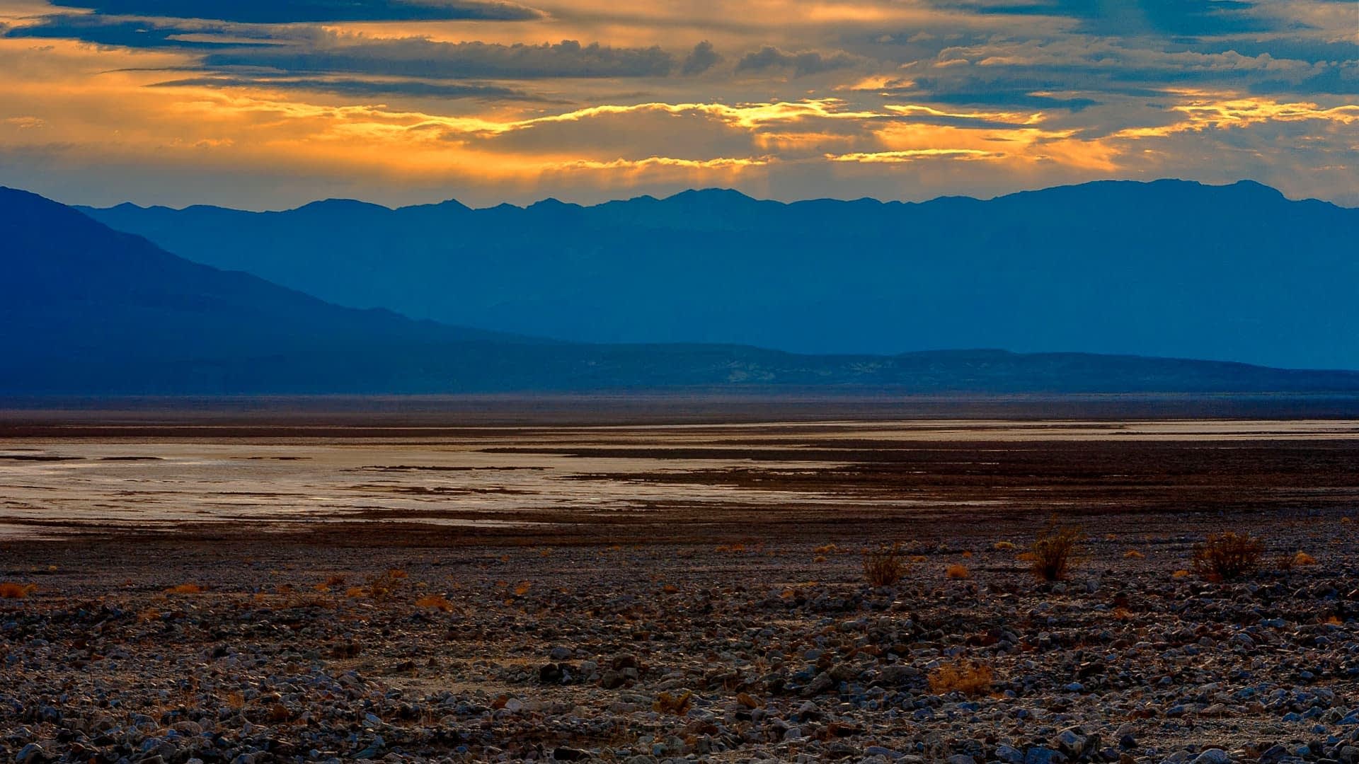 A desert landscape featuring mountains and a sunset with clouds in the sky. - Olive Oil Times