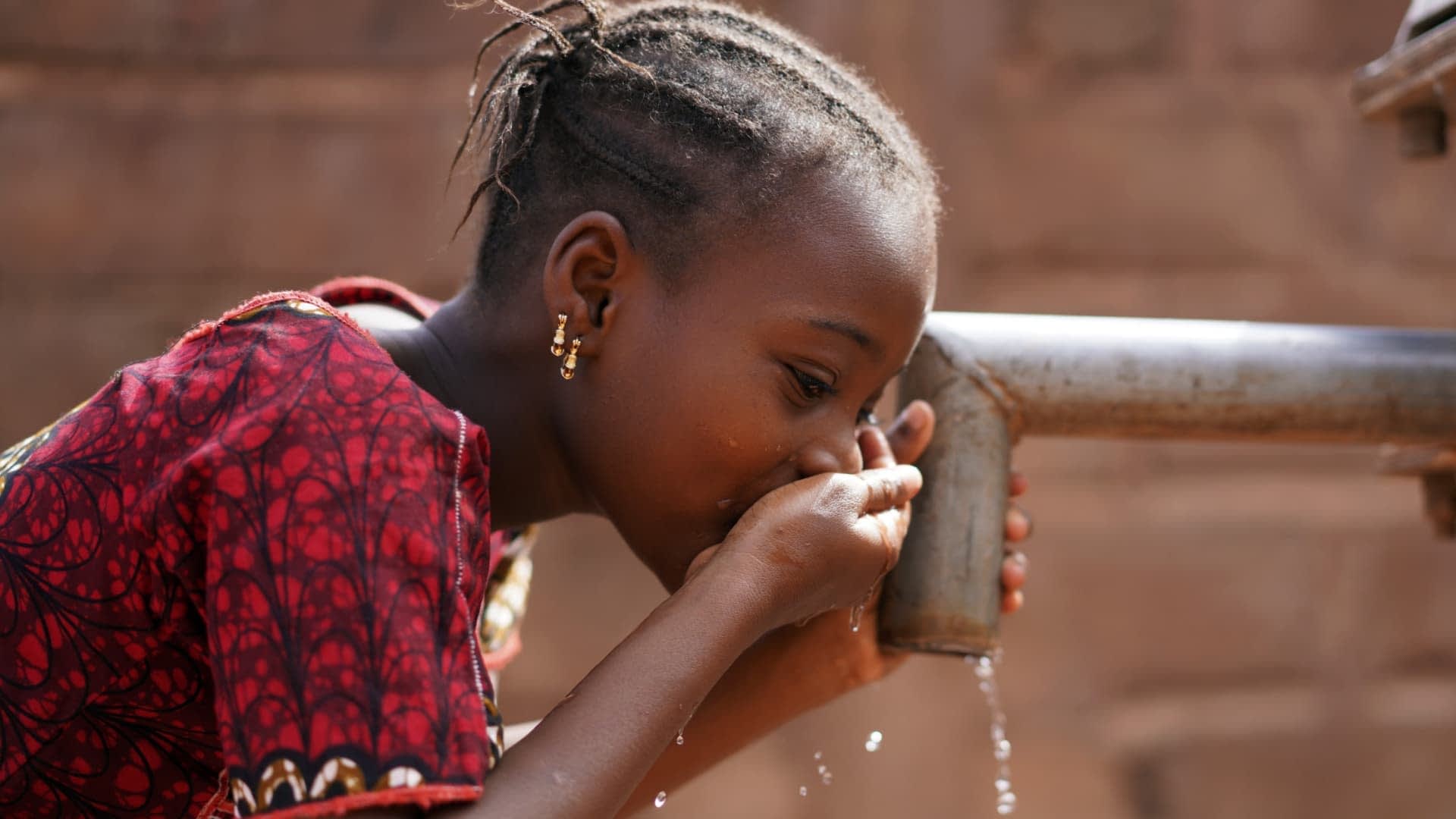 A child drinking water from a tap using cupped hands in a close-up view. - Olive Oil Times
