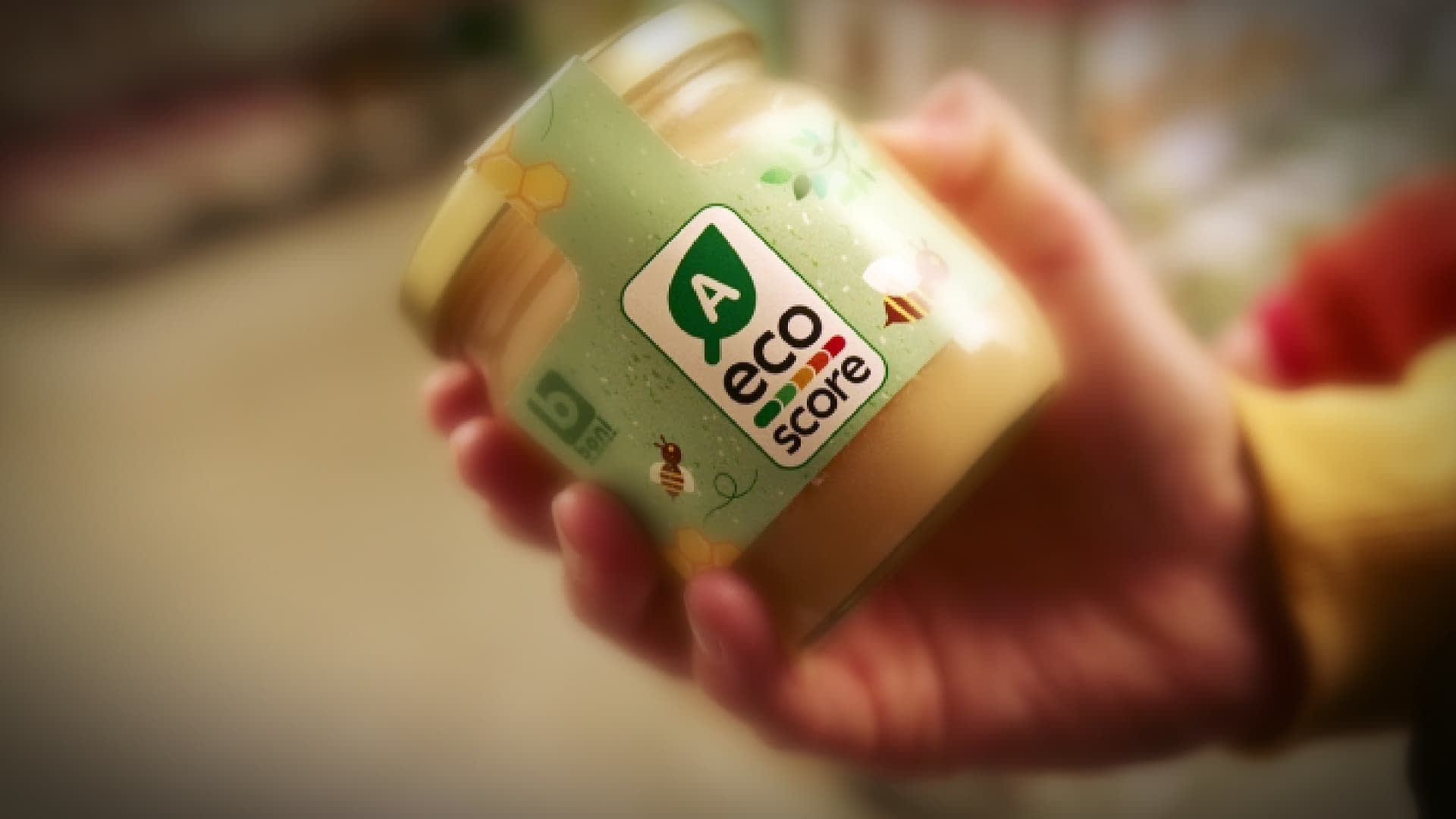 Hand holding a jar labeled with an eco score rating and a green logo. - Olive Oil Times