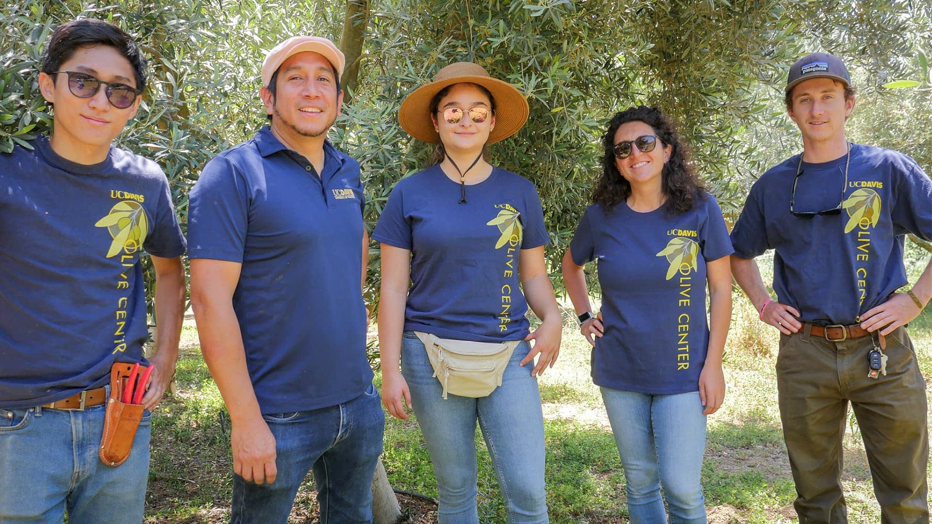 Five individuals wearing matching shirts standing together at an olive center. - Olive Oil Times